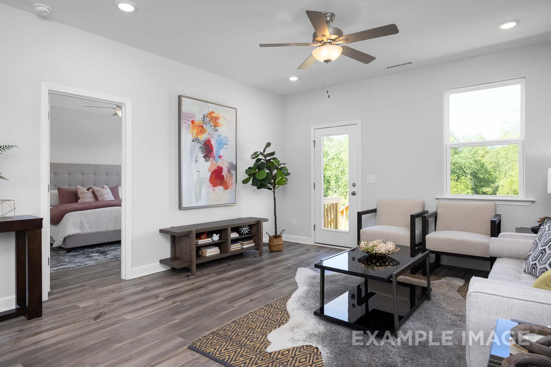 Spacious living room in The Carter B master suite with ceiling fan, abstract wall art, fiddle leaf fig, beige sofa, and deck view