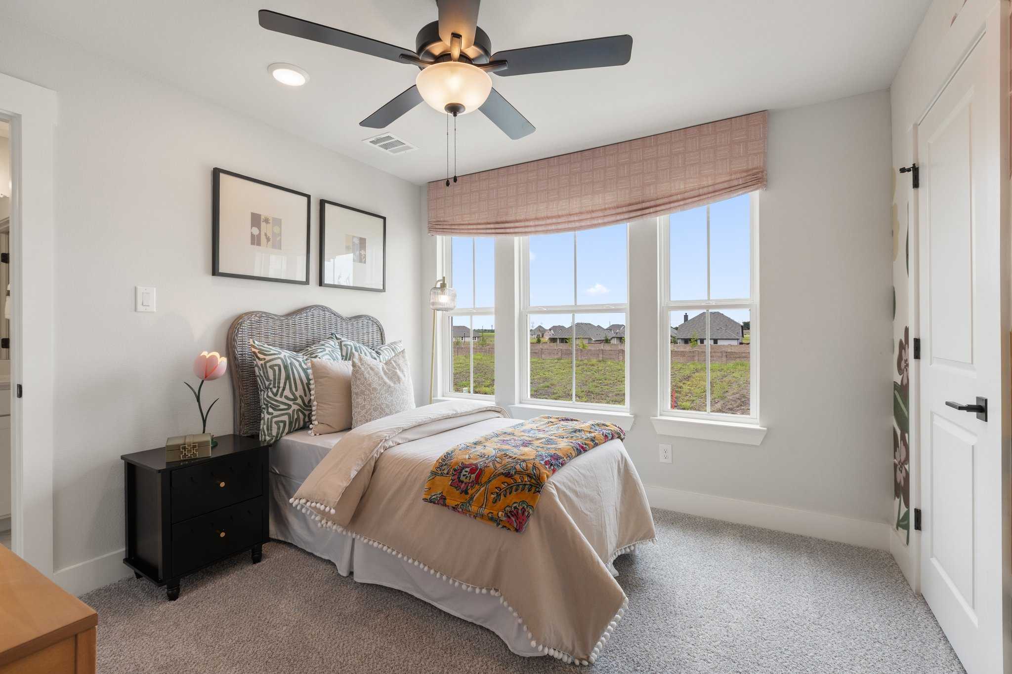 Cozy bedroom interior at Mercer Meadows in Royse City Texas with wicker headboard bed, colorful quilt, and scenic field views through windows