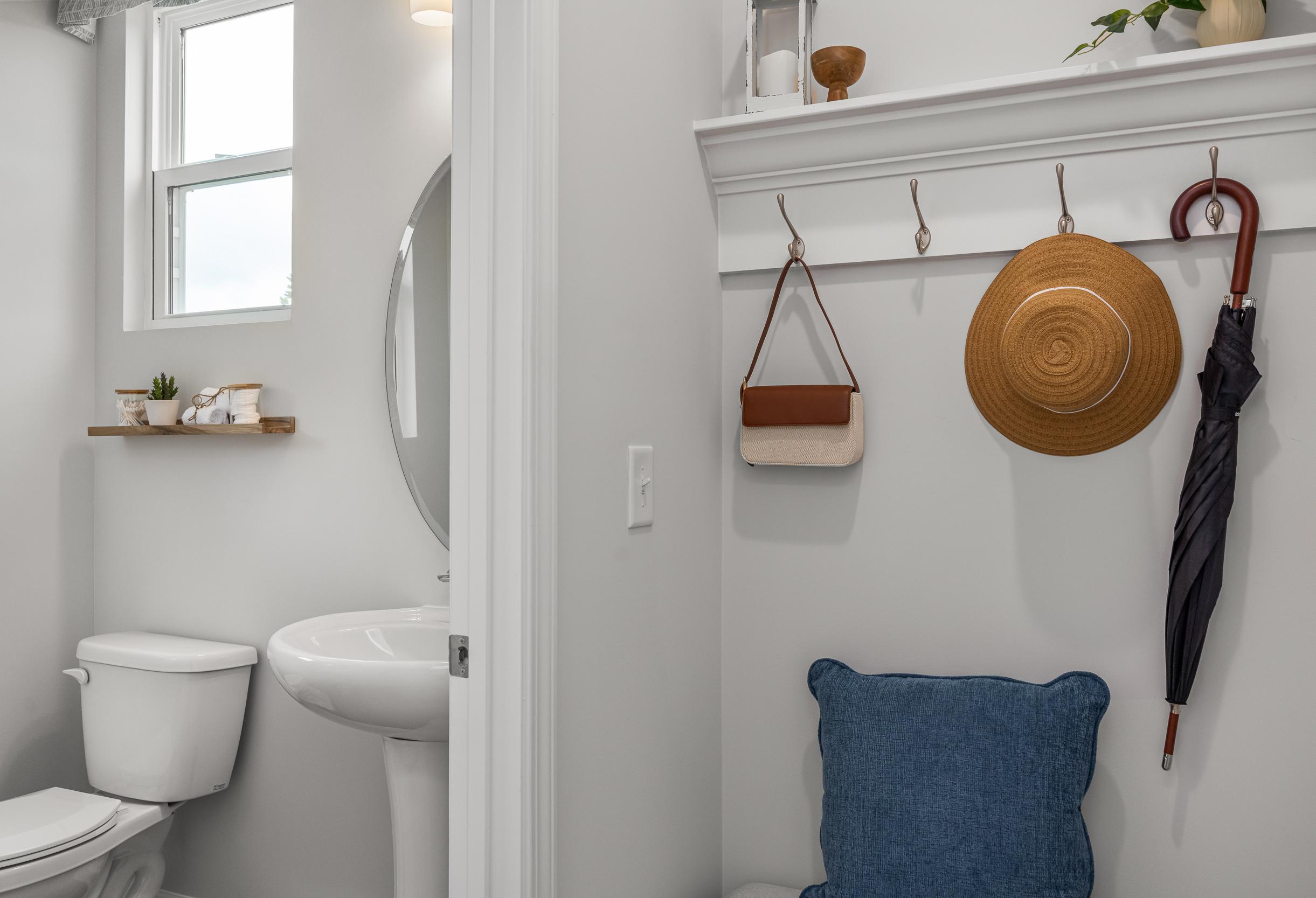 Mudroom entry with coat rack and bench seating adjacent to a half bath in The Graham home design.