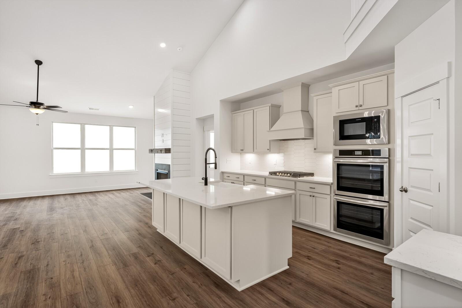 Modern open-concept kitchen with white shaker cabinets, large quartz island, stainless double ovens, and shiplap accents in Davidson Homes The Ridgeport C, Gallatin, TN