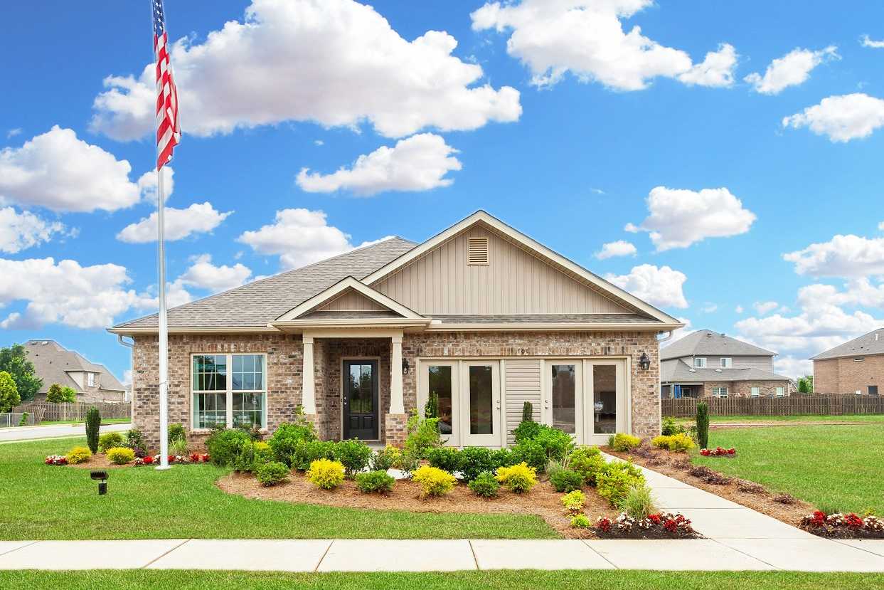 Beige brick home exterior at Williams Pointe in Huntsville Alabama with American flag, covered porch and landscaped front yard