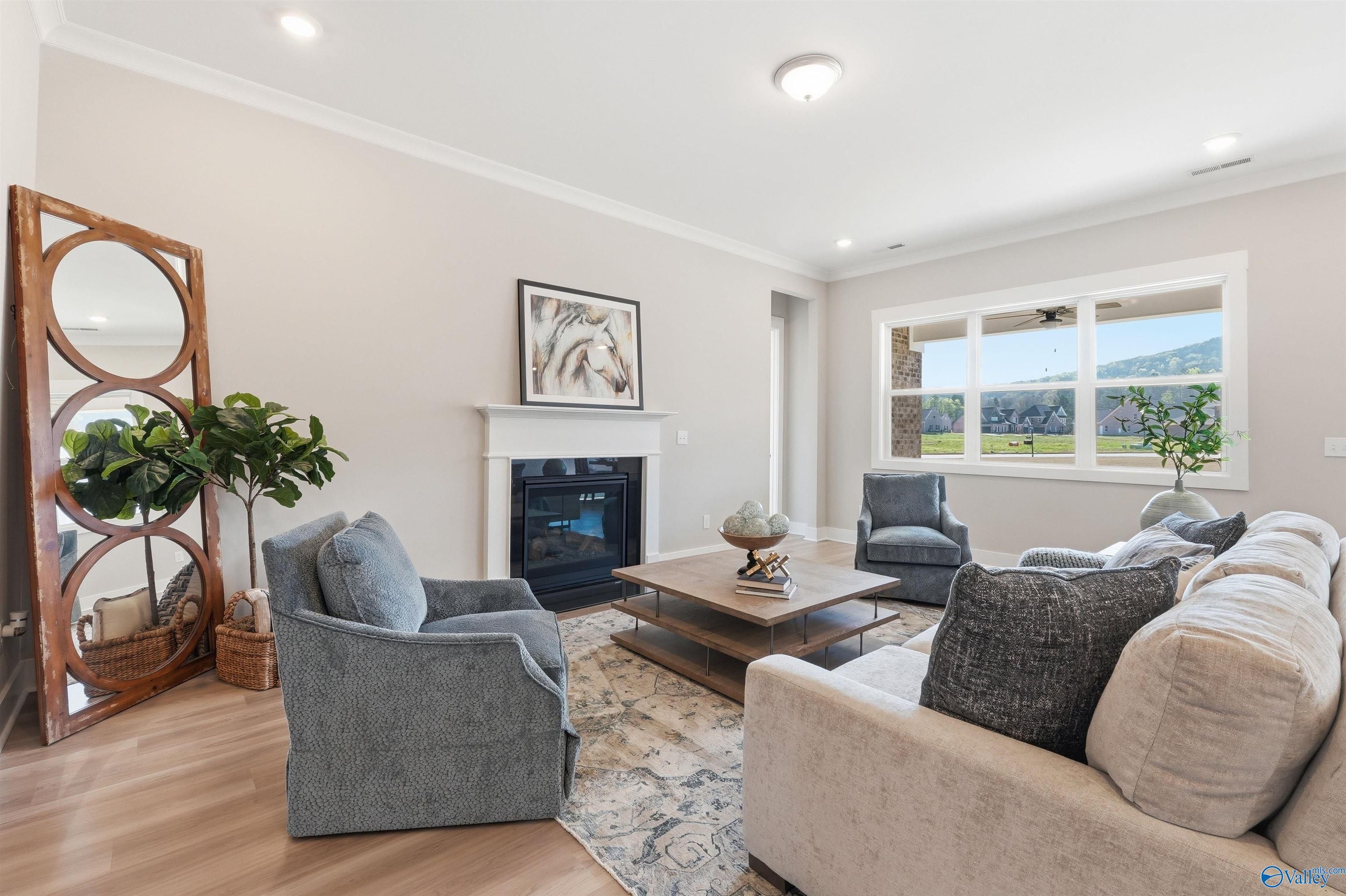 Cozy living room with gas fireplace, blue velvet armchairs, beige sofa, and mountain view windows in Evermore Homes The Oxford B, Owens Cross Roads, Alabama