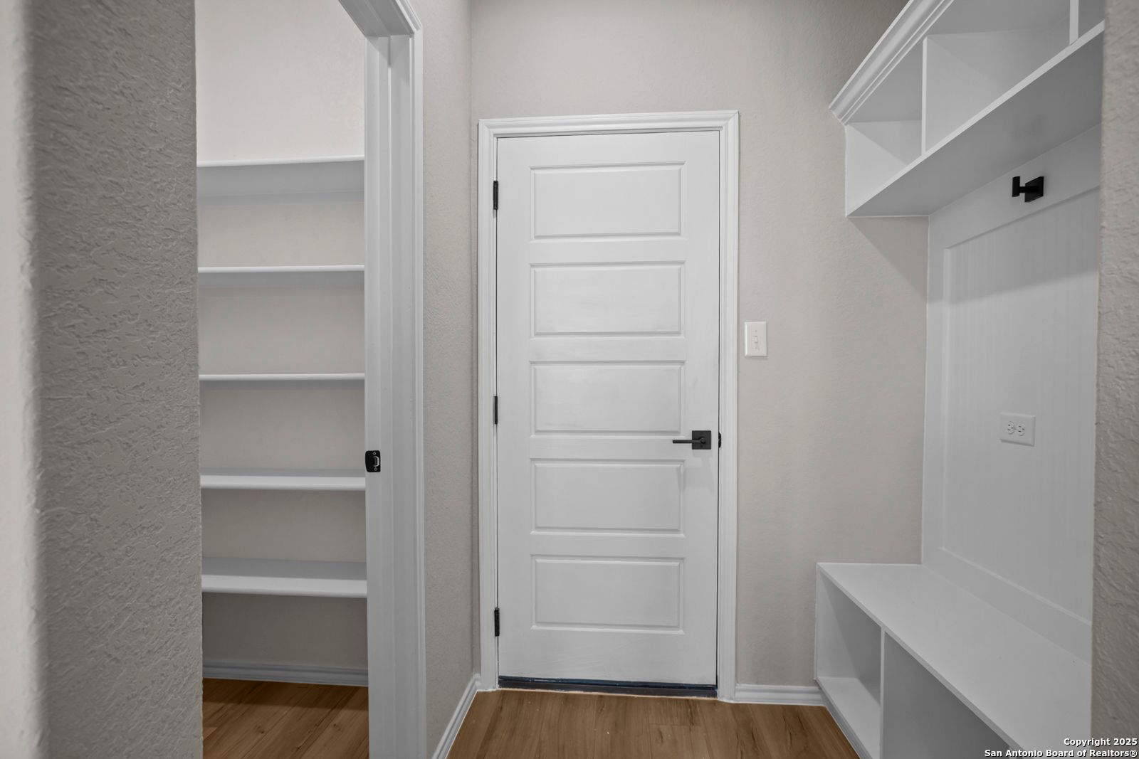 Spacious mudroom with built-in white bench, open shelves, hooks, and paneled door in Davidson Homes Sequoia A, Converse Texas