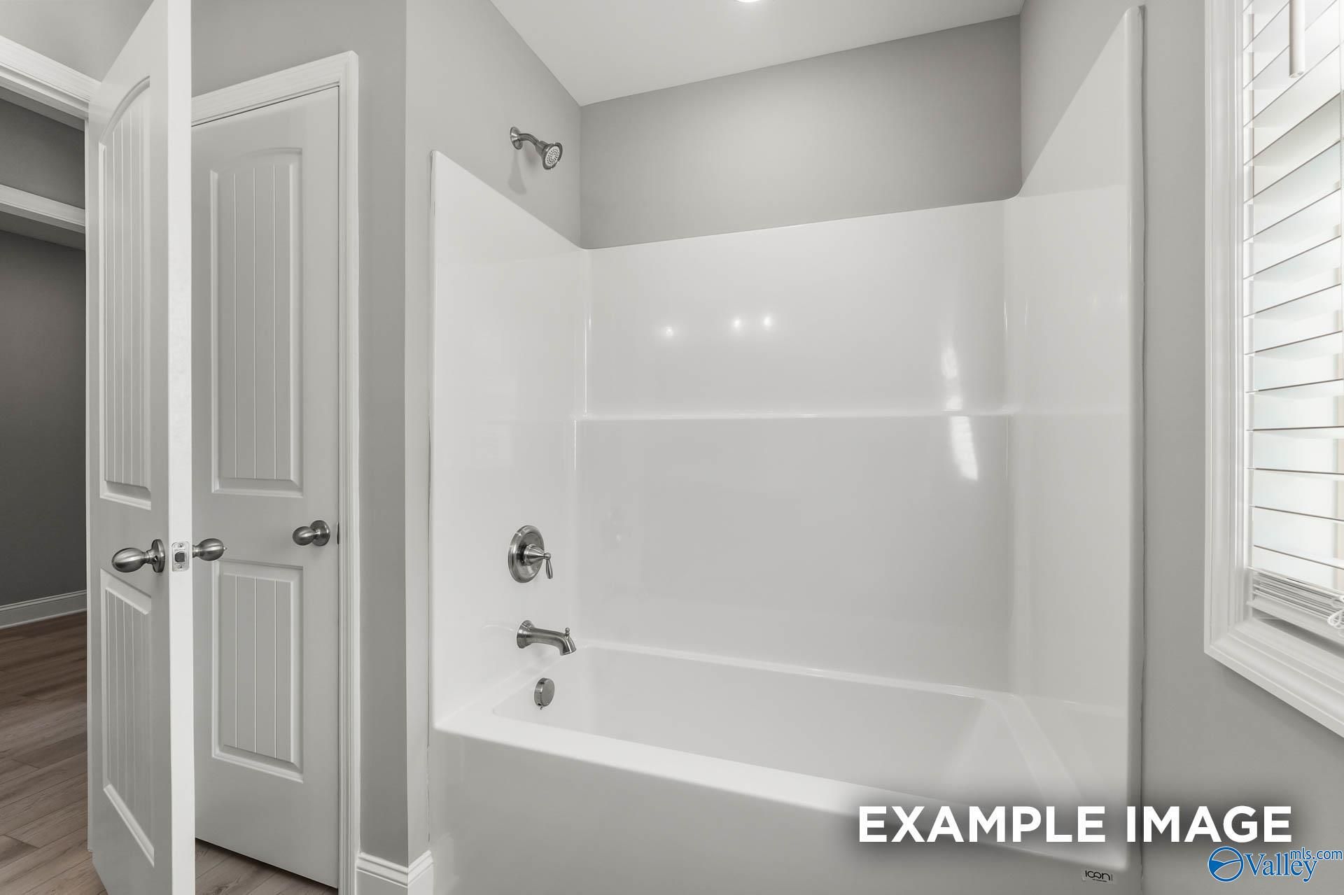 White bathtub-shower combo with chrome fixtures and glass doors in modern bathroom, The Everett B by Davidson Homes, Toney AL