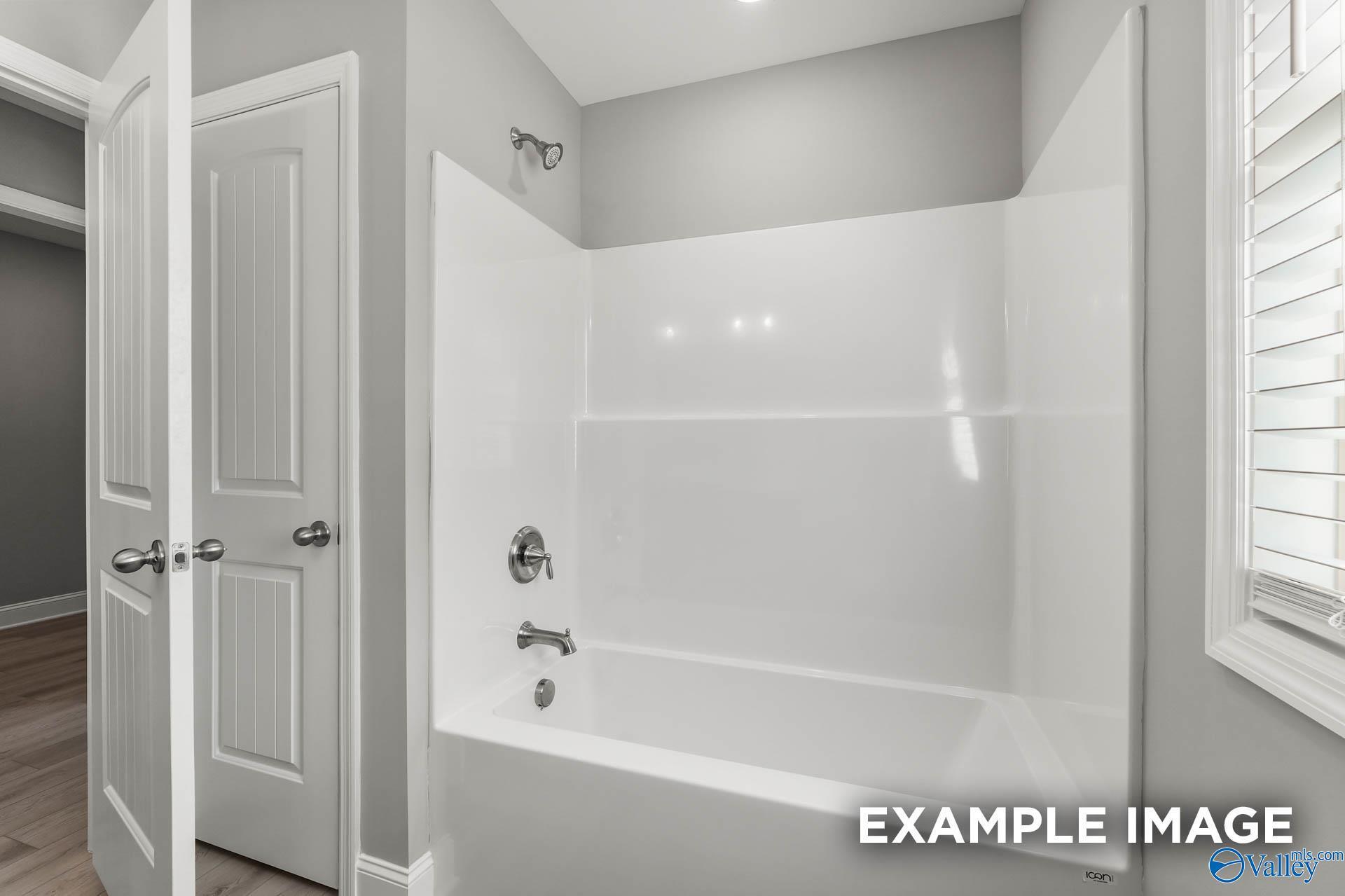 White bathtub-shower combo with chrome fixtures and glass doors in modern bathroom, The Everett B by Davidson Homes, Toney AL