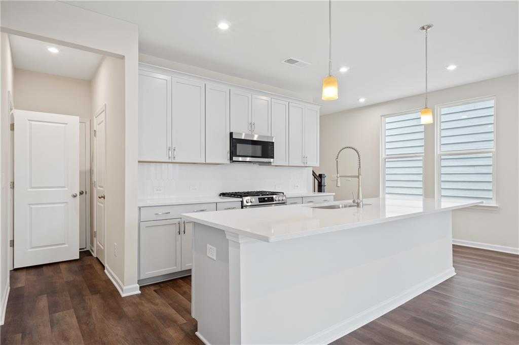 Modern white kitchen with stainless steel appliances, quartz island, and hardwood floors in Davidson Homes The Cary B, Kennesaw, GA