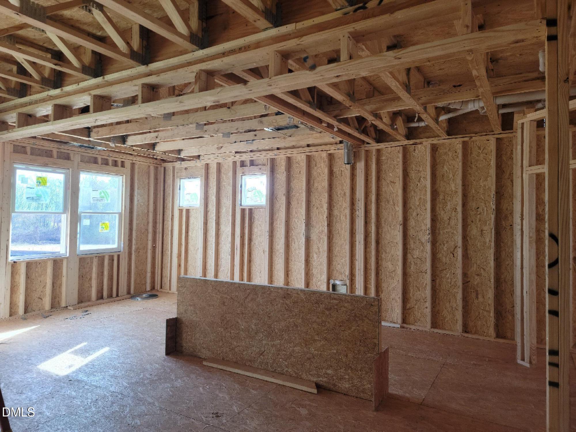Framed interior with exposed wooden trusses, plywood walls, and large windows in The Cypress B II home by Davidson Homes, Angier, NC