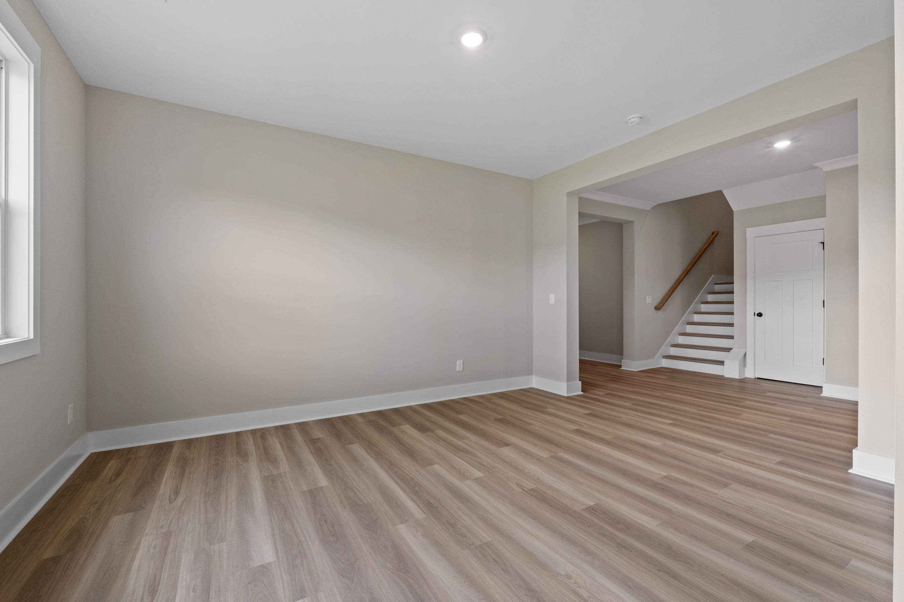 Spacious foyer in The Oxford B with light hardwood floors, beige walls, large window, and open archway to staircase