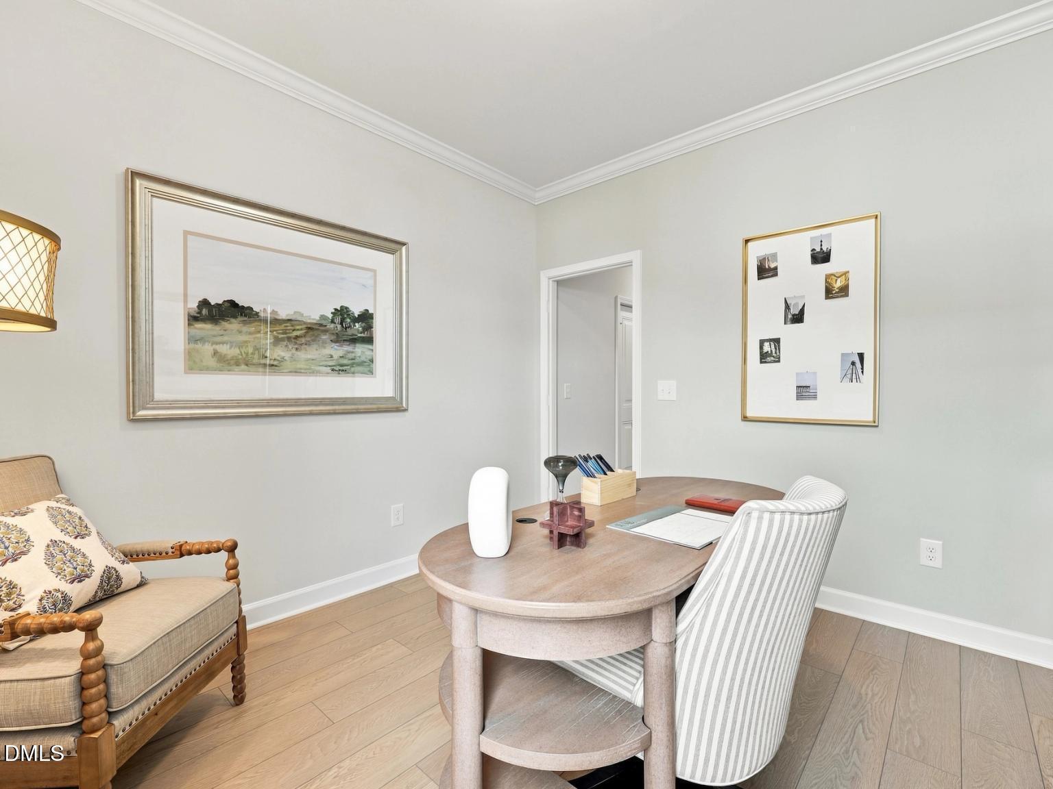 Bright home office with wooden desk, striped chair, and framed wall art in The Daphne C floor plan, Woodland Crossing.