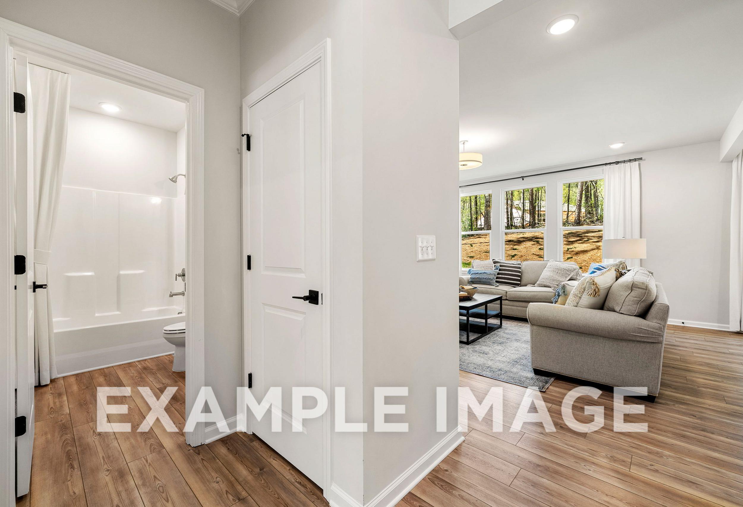 The Hickory B interior: white bathtub and shower in modern bathroom adjacent to living room with beige sofa and large windows