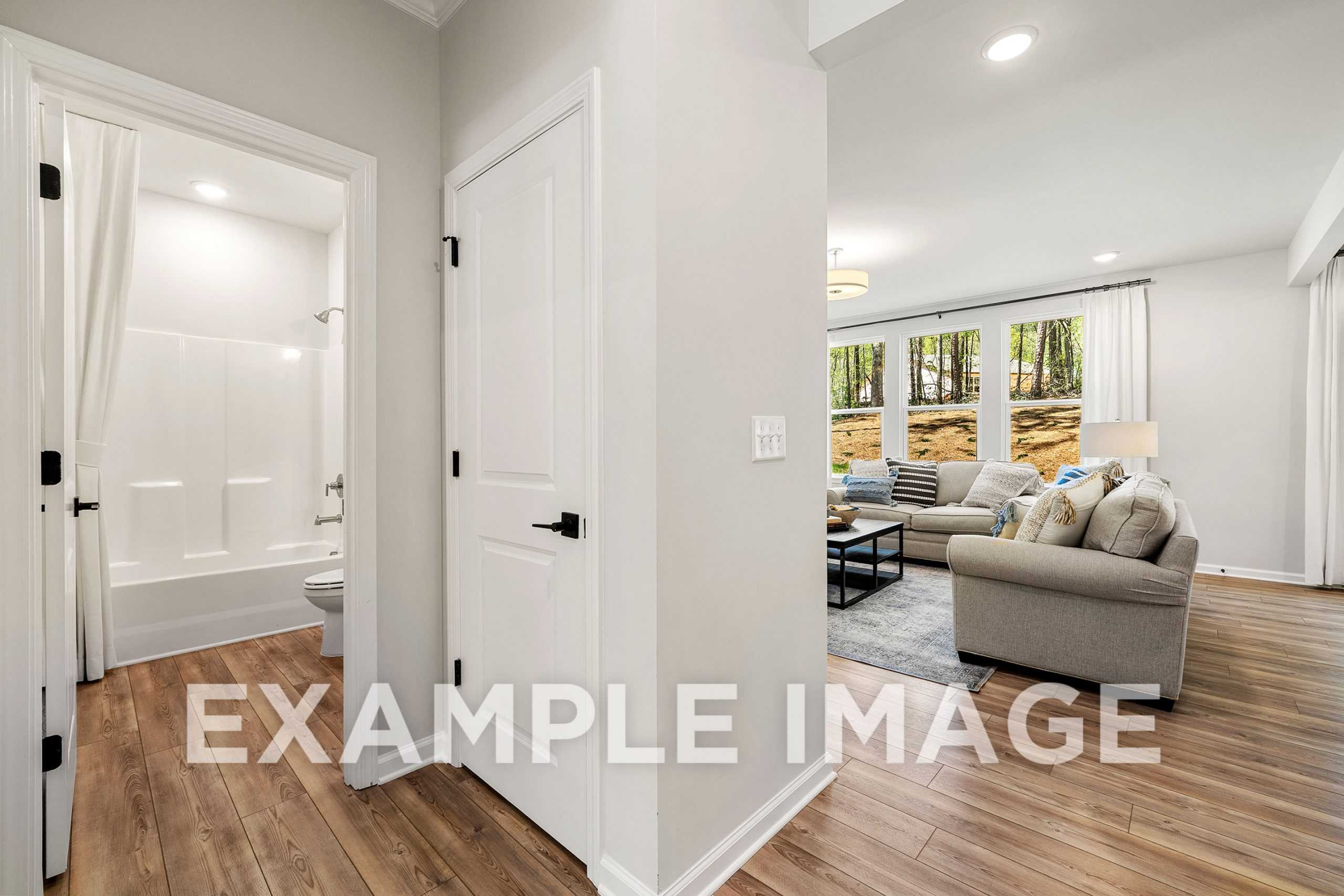 Interior of The Hickory A home design featuring white bathtub bathroom and open living room with beige sofa, wood floors, large windows