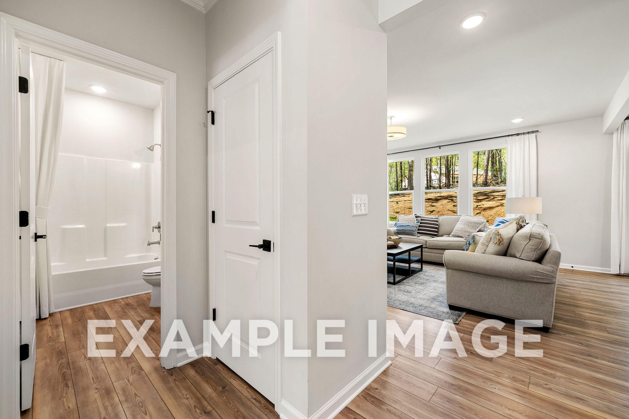 The Hickory B interior: white bathtub and shower in modern bathroom adjacent to living room with beige sofa and large windows