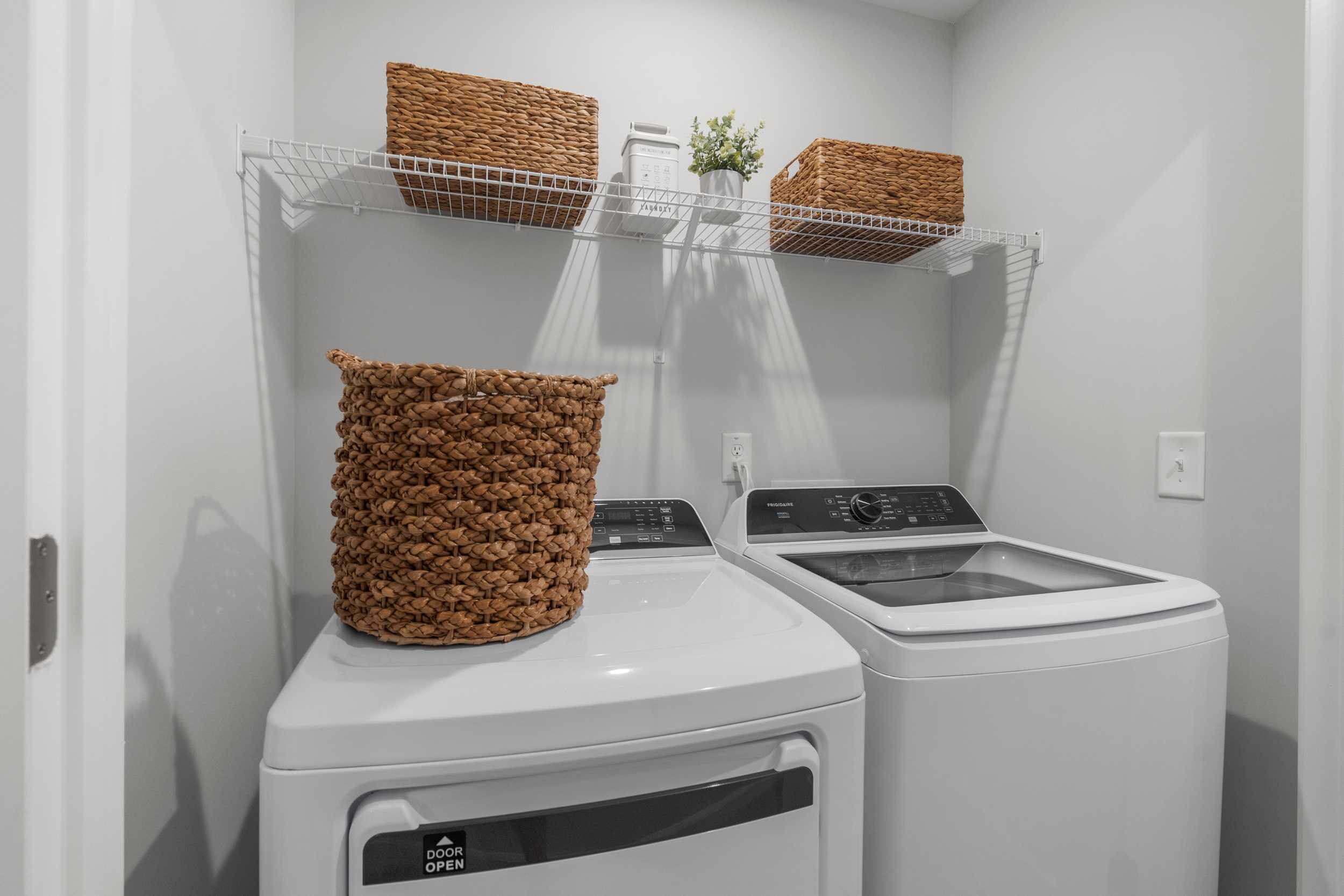 Modern laundry room in Stegall Village Emerson GA with white washer dryer, wire shelves, and wicker baskets