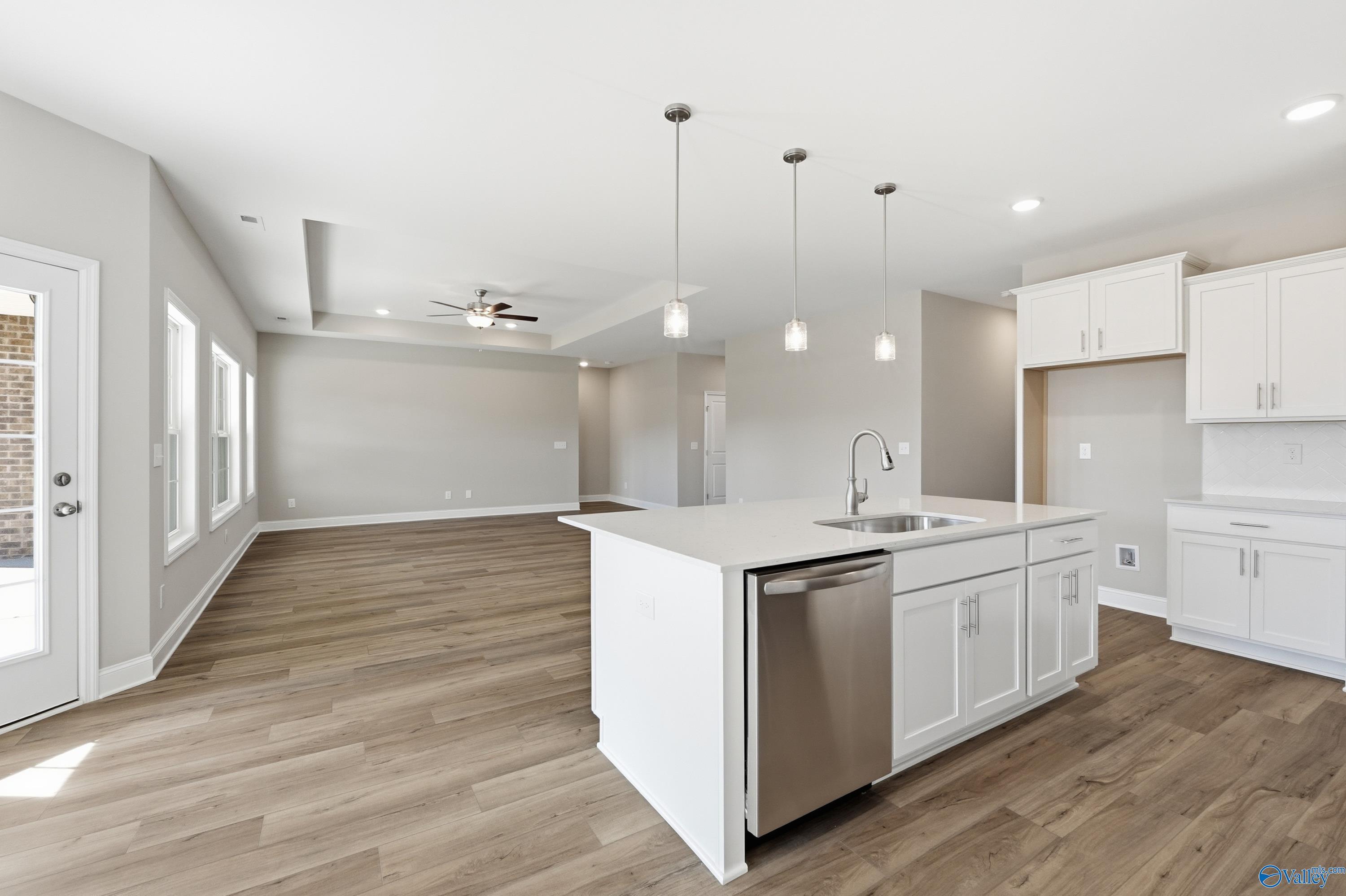 Modern open-concept kitchen with white island, stainless dishwasher, and hardwood floors in Davidson Homes The Rockford, Harvest, Alabama