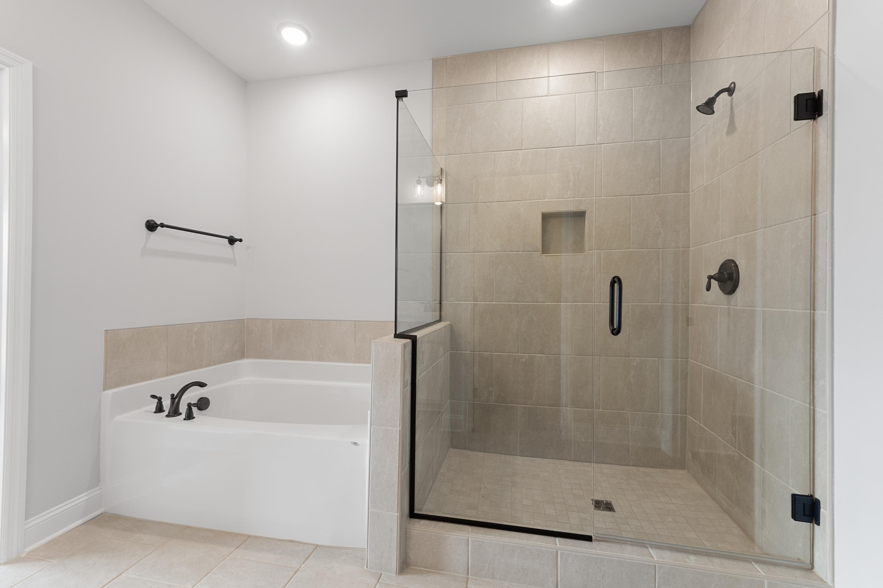 Spacious master bathroom in The Copeland with glass-enclosed shower, freestanding soaking tub, and modern black fixtures