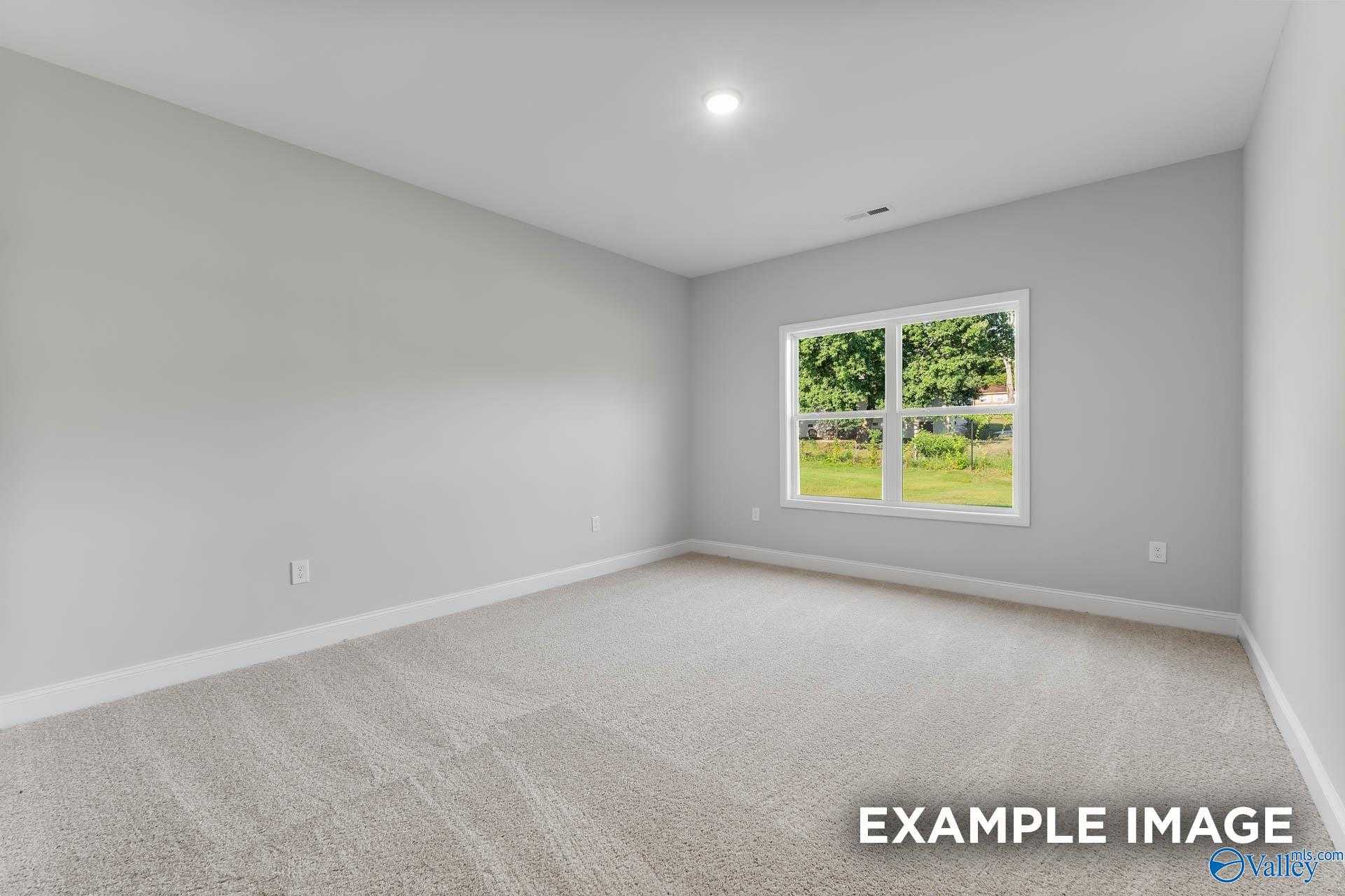Bright empty bedroom with gray walls, carpet floor, and large window overlooking lush green yard in Davidson Homes The Daphne C, New Market, AL