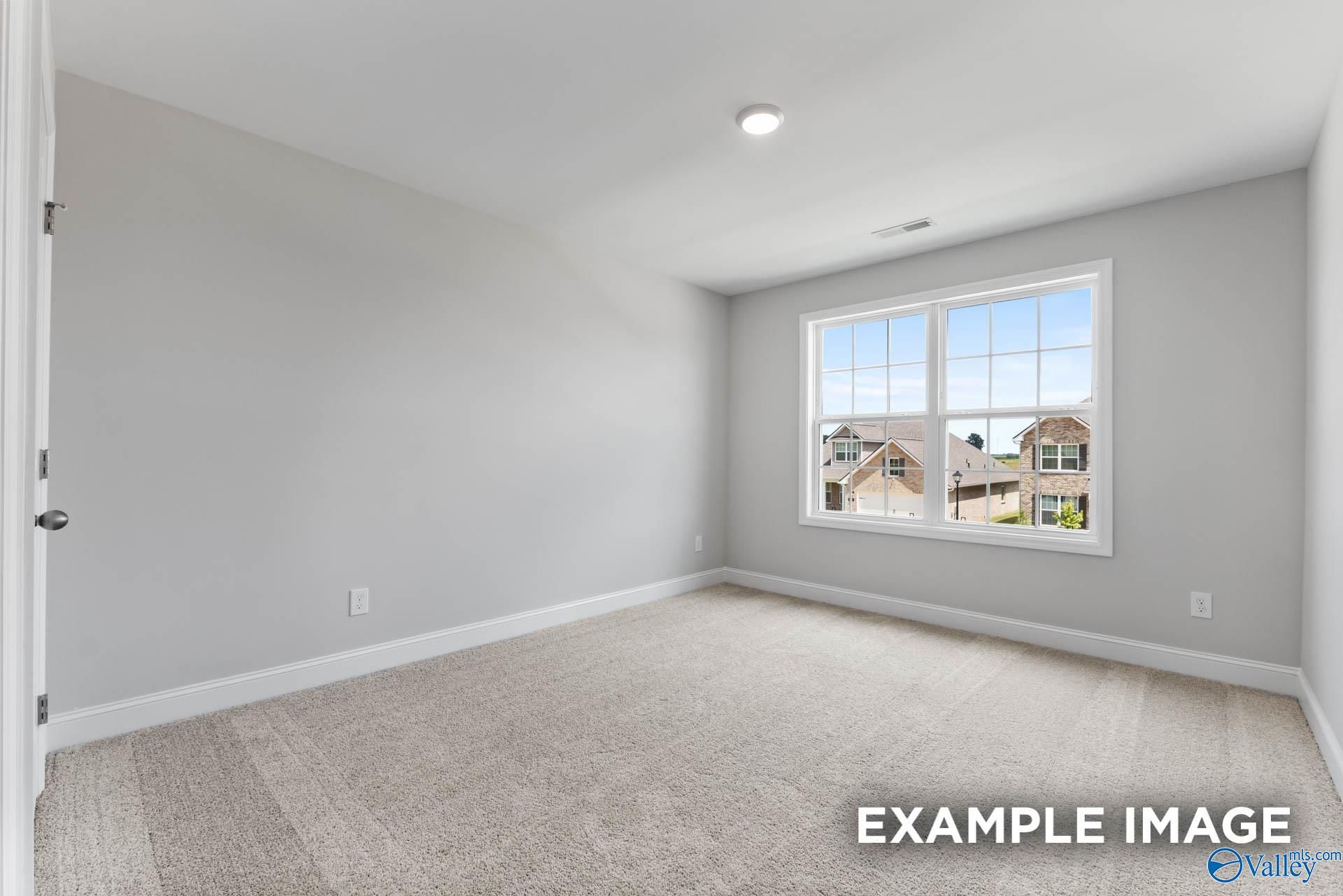 Bright secondary bedroom with gray walls, large window overlooking neighborhood, and carpeted floor in 5-bedroom The Madison A home in Meridianville, Alabama
