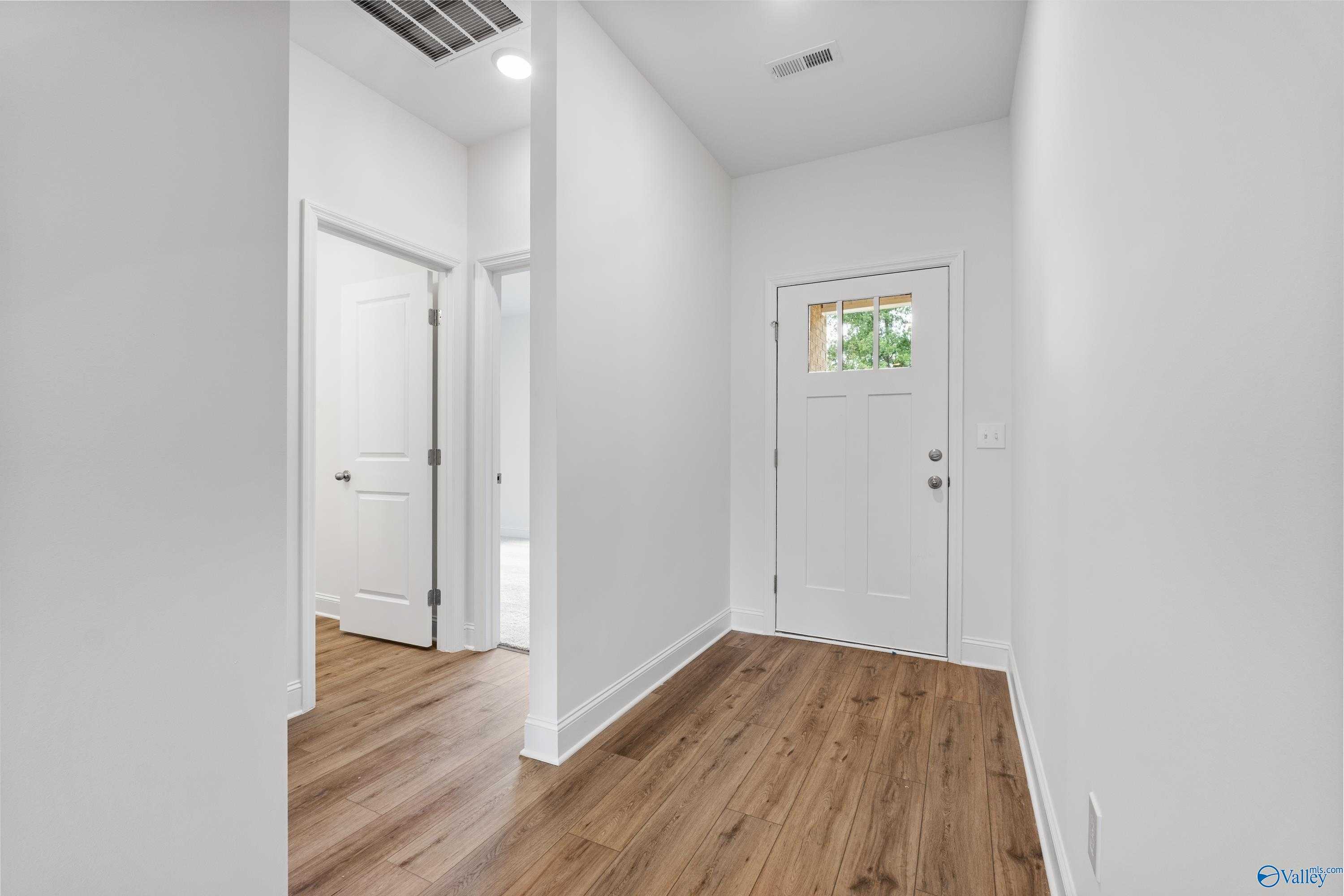 Bright entry hallway with hardwood floors, white doors, and front entry door in 3-bedroom Davidson Homes The Asheville C, New Market, Alabama