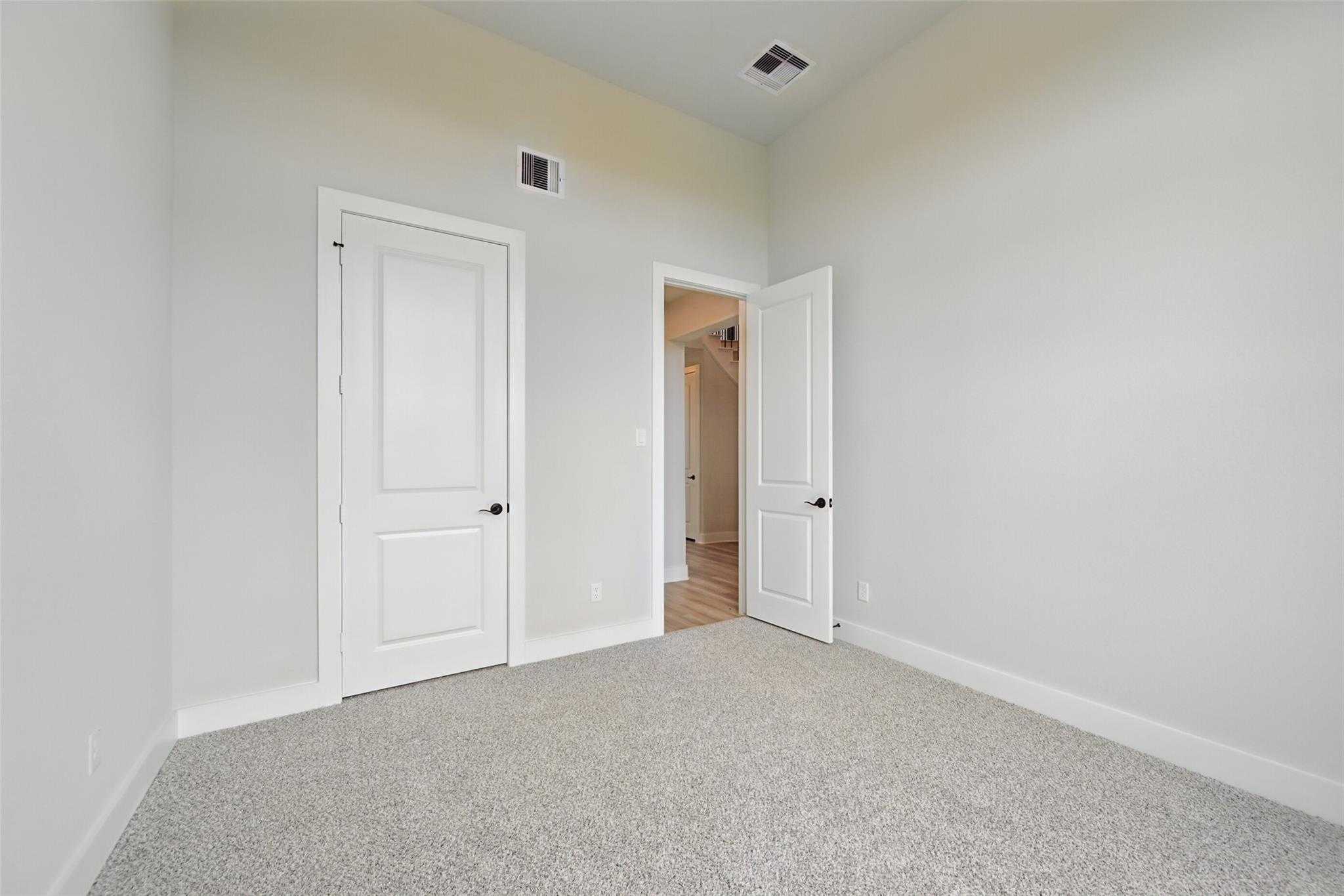 Spacious empty bedroom with gray carpet, white paneled doors, and adjacent bath in 4-bed Davidson Homes Victoria C, Lago Mar, Texas City