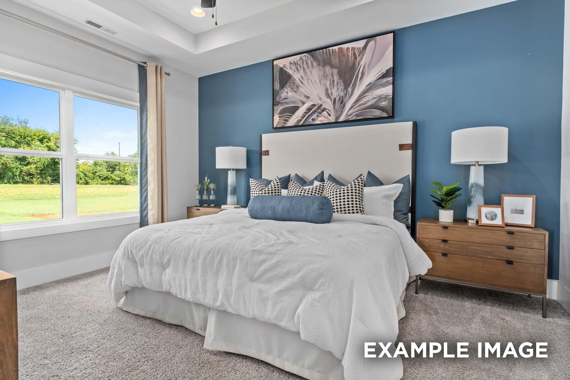Spacious master bedroom in The Franklin C with blue accent wall, king bed, abstract art, and scenic green field view