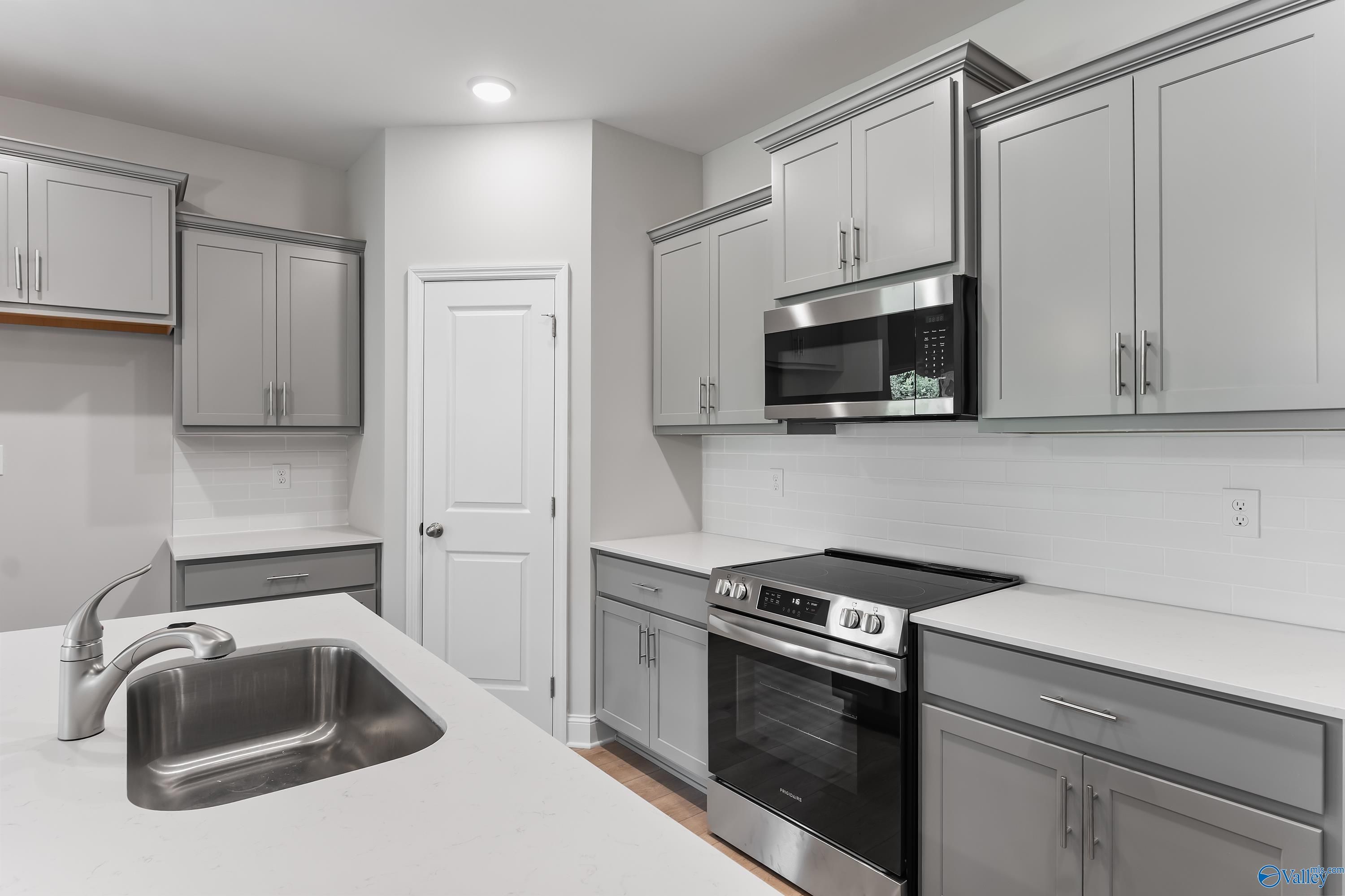 Modern gray shaker kitchen with stainless steel appliances, large farmhouse sink, and white quartz counters in Davidson Homes The Daphne C, Huntsville