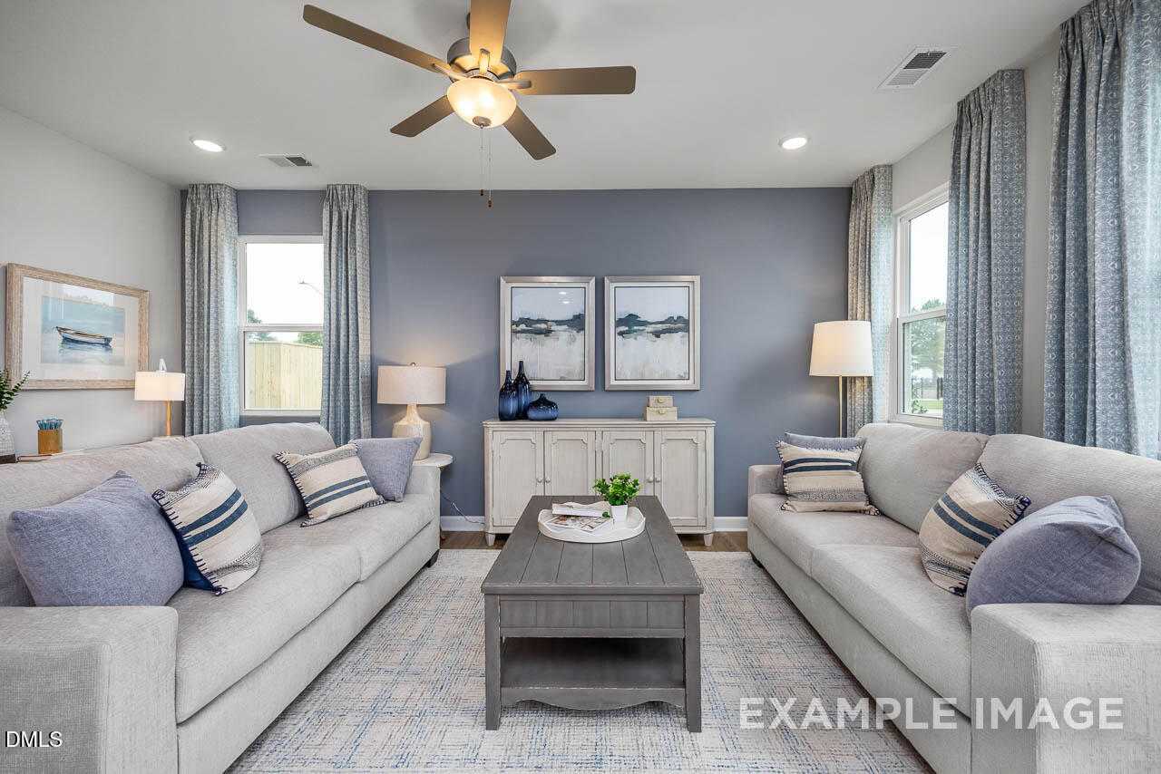 Cozy living room with gray sofas, blue accent wall, coastal art, and ceiling fan in Davidson Homes The Graham Exterior, Fuquay-Varina, NC