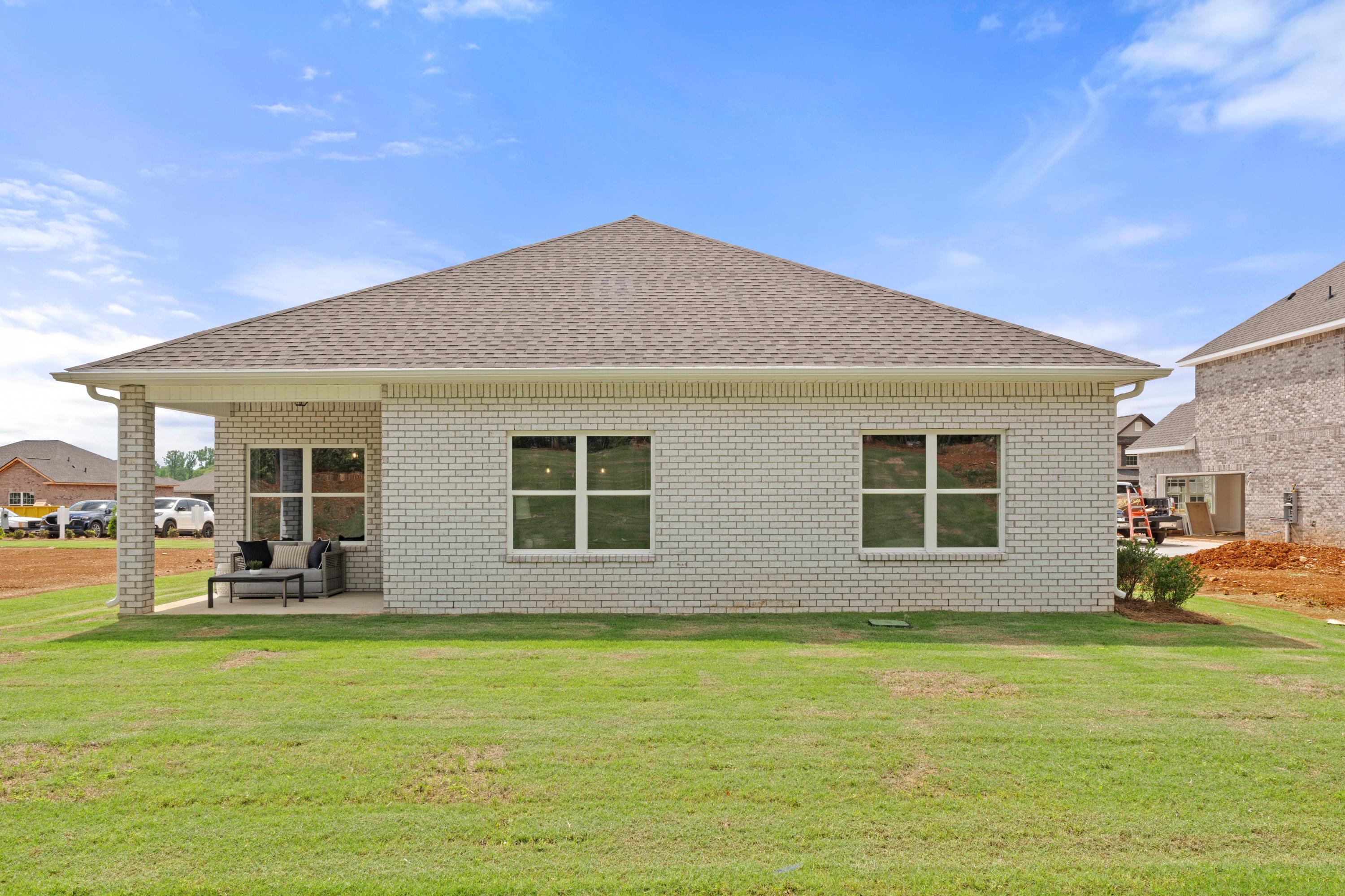 Side view of beige brick home at Ivy Hills in Toney, Alabama with covered porch, windows, and green lawn