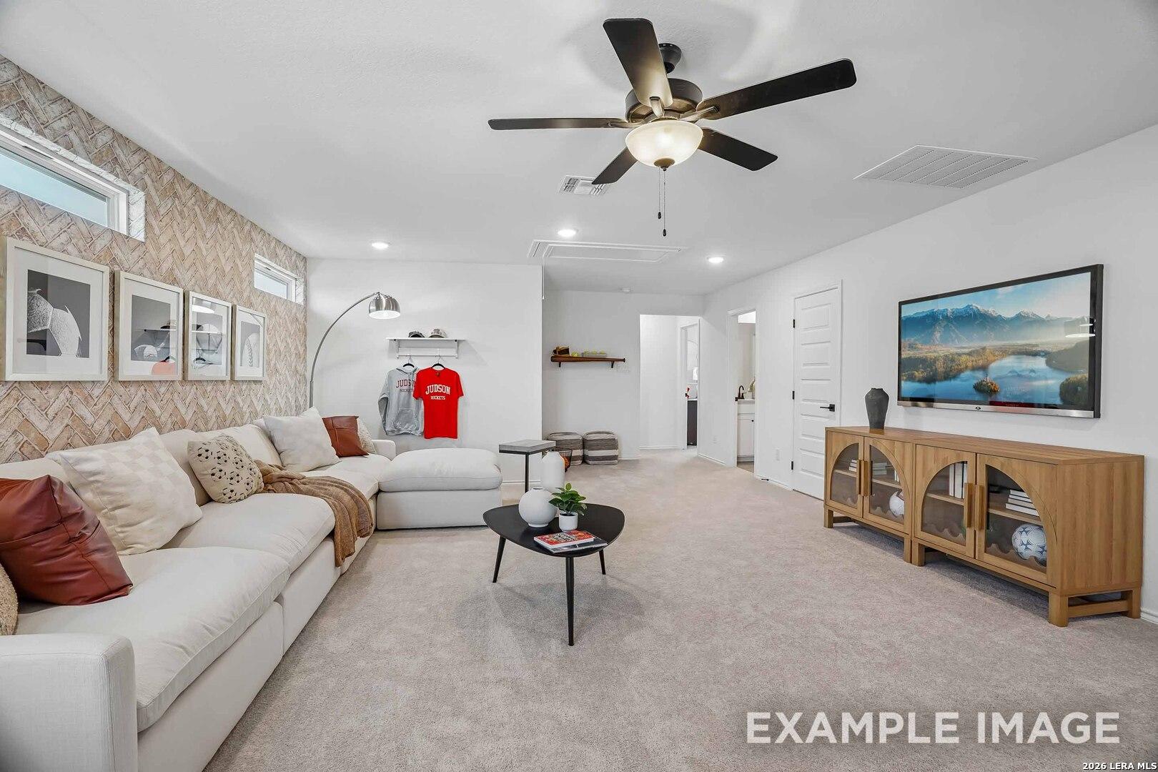 Bright family room with white sectional sofa, brick accent wall, ceiling fan, and mounted TV in Davidson Homes' Pinecrest F floor plan, San Antonio