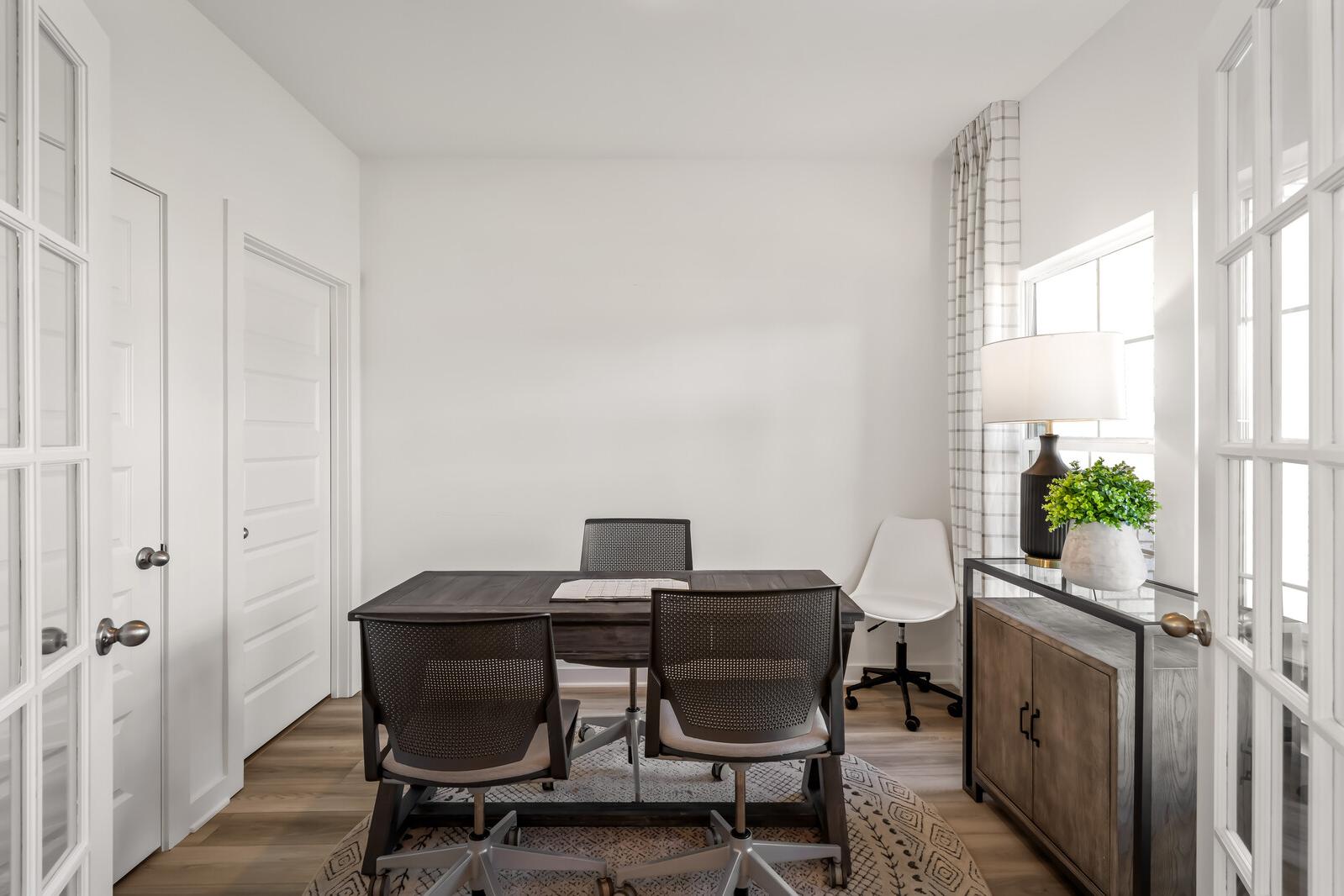 Modern home office at The Towns at Red River in Gallatin TN featuring wooden desk, mesh chairs, plant, and French doors