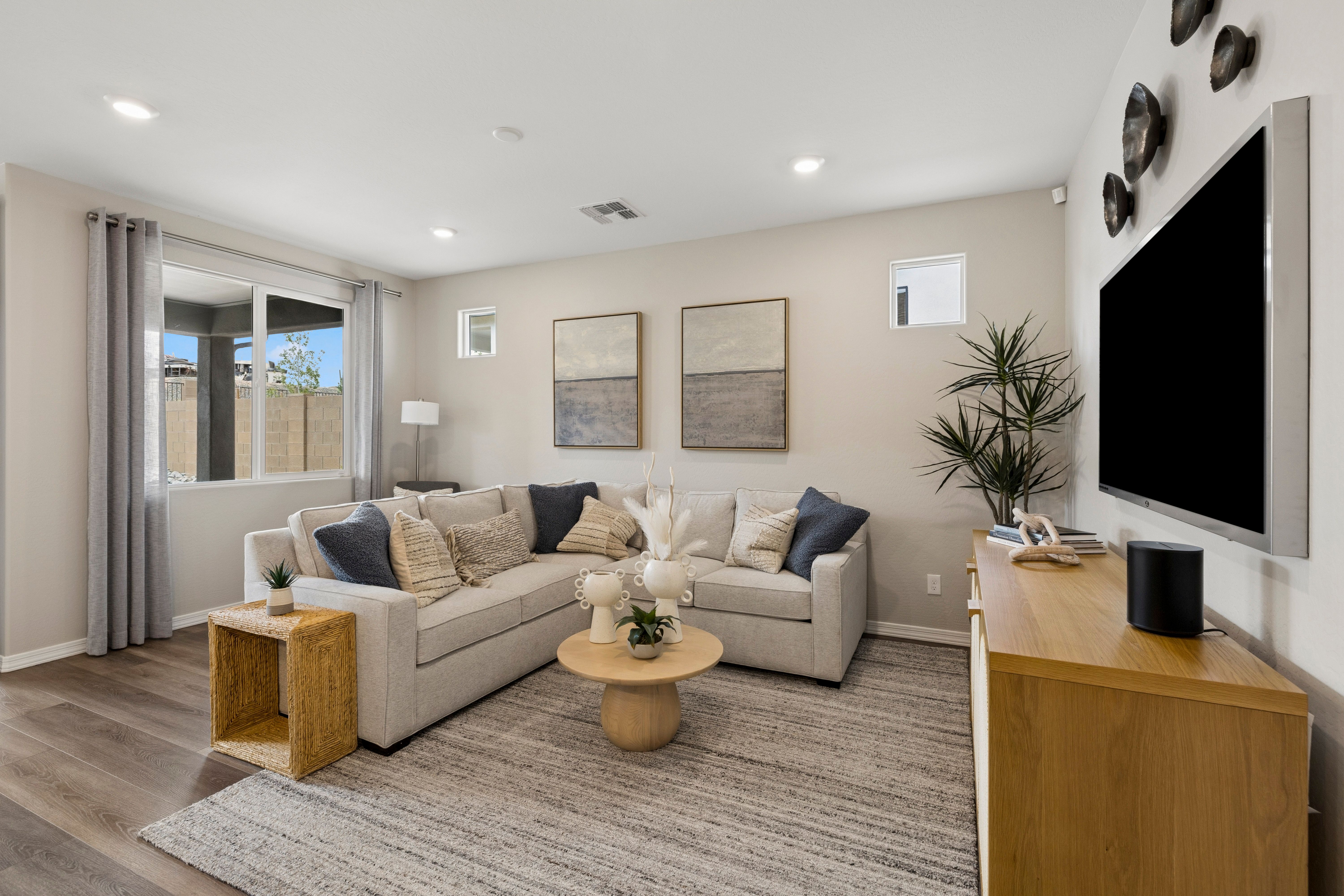 Cozy modern living room at South Ranch in Prescott AZ by Davidson Homes with beige L-shaped sofa, abstract art, plants, and hardwood floors