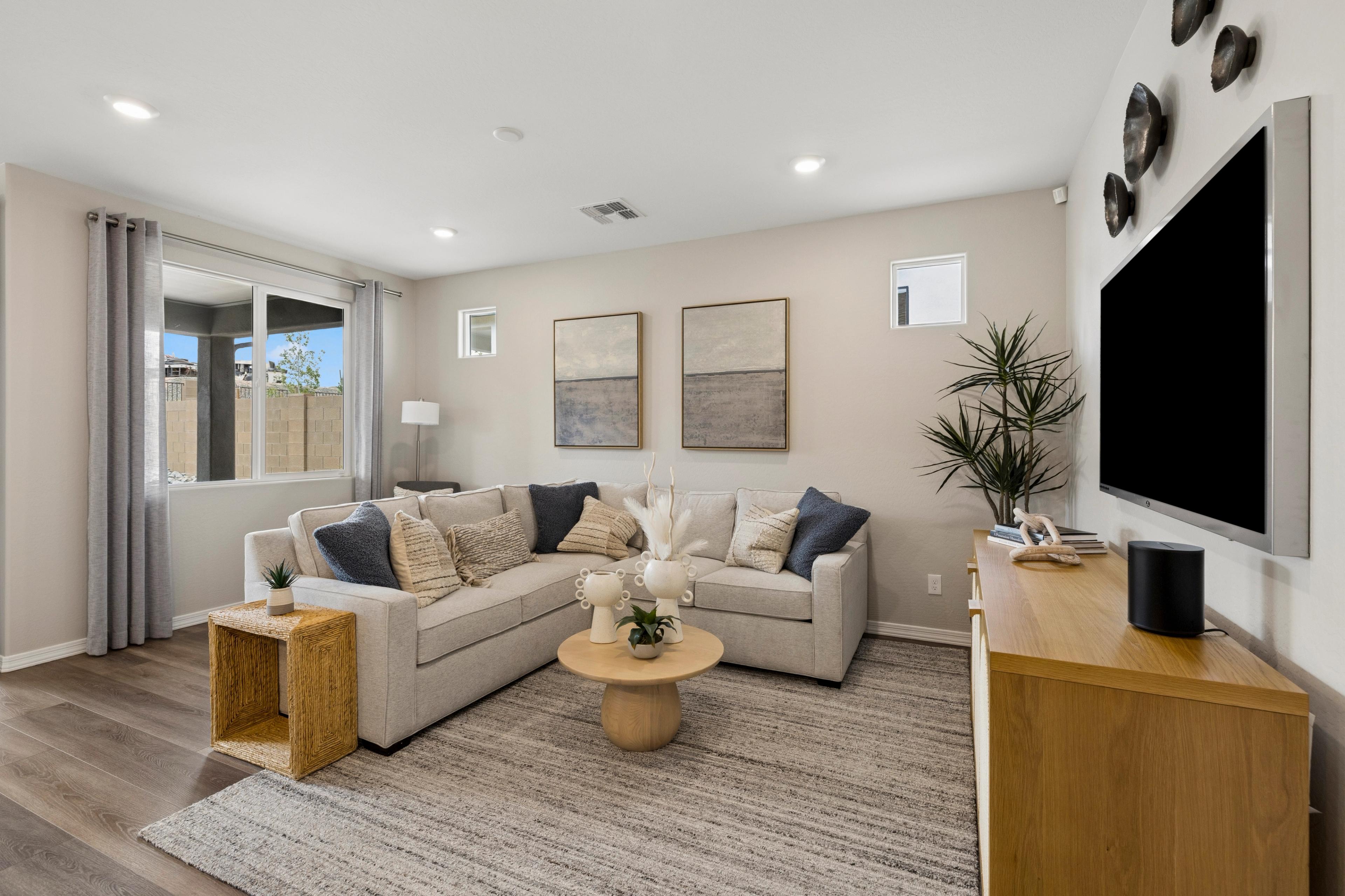Cozy modern living room at South Ranch in Prescott AZ by Davidson Homes with beige L-shaped sofa, abstract art, plants, and hardwood floors