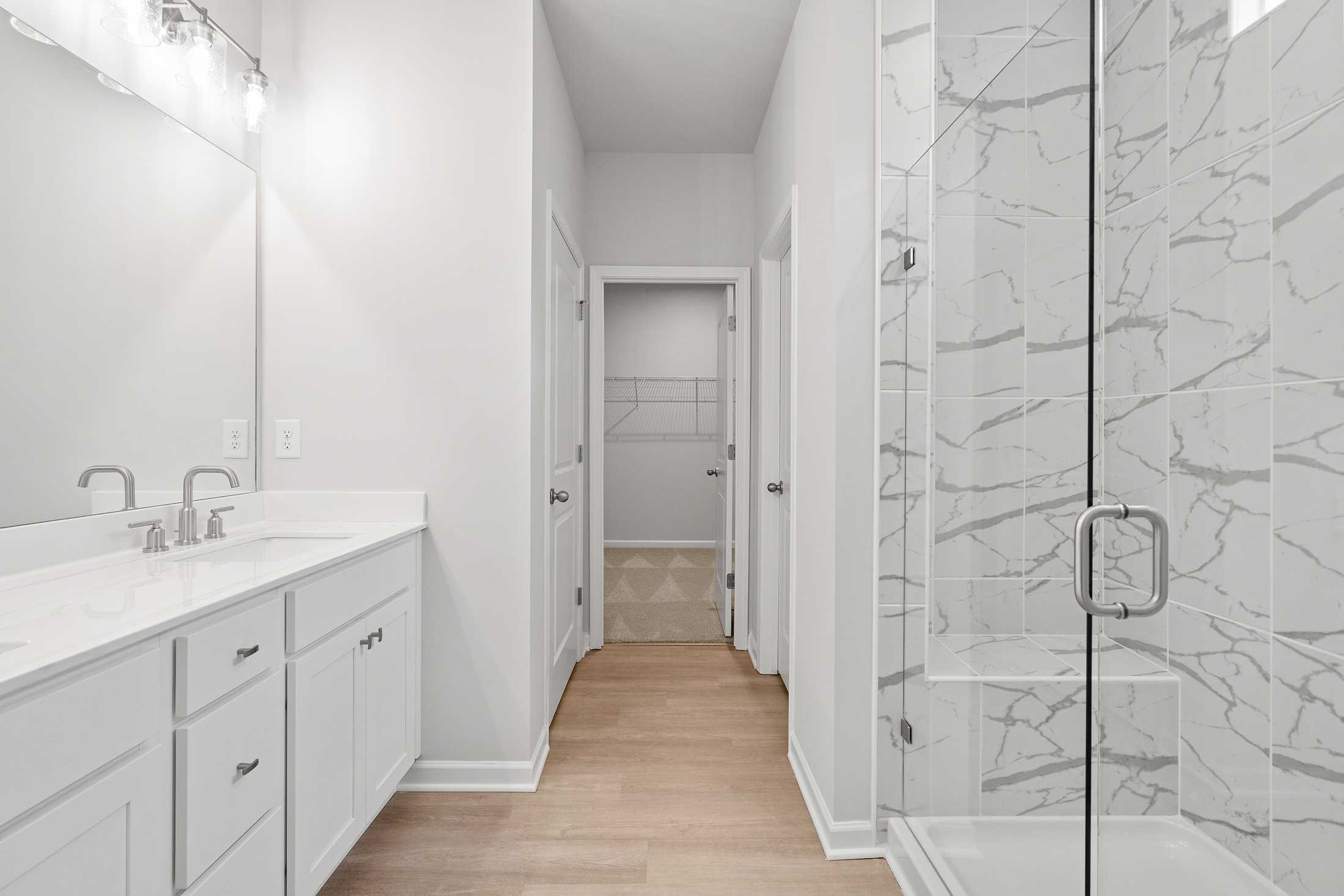 Spacious master bathroom in The Ash B featuring double vanity, frameless glass shower with marble-look tile, white cabinetry