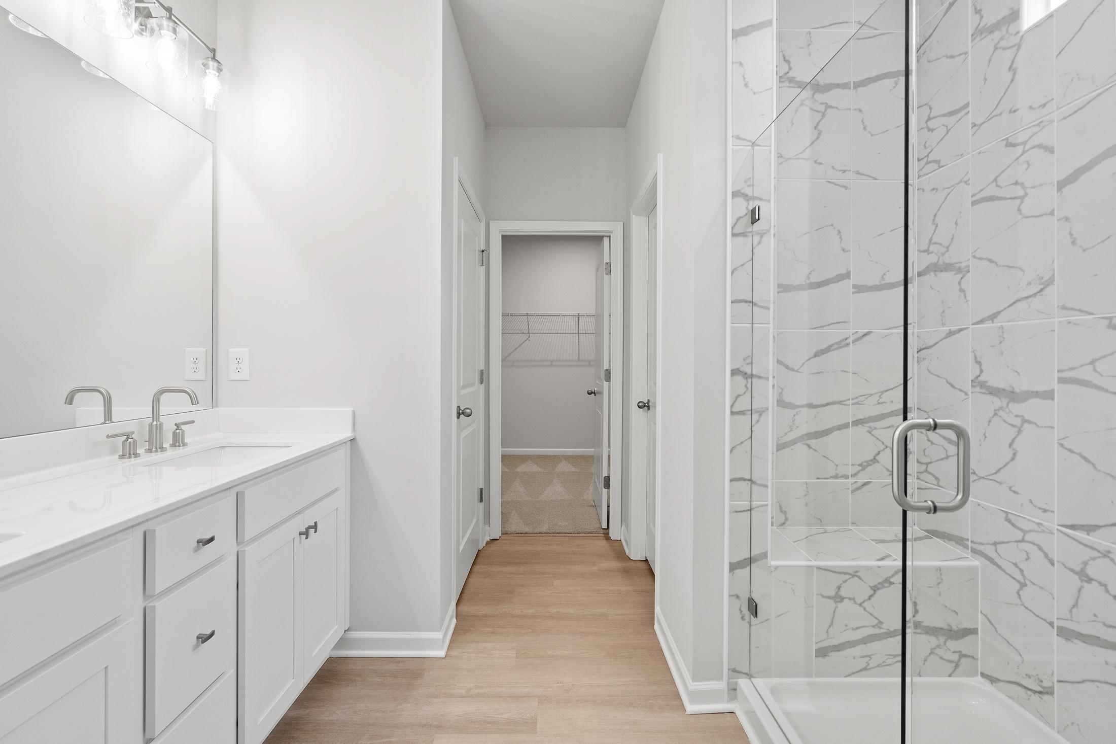Spacious master bathroom in The Ash B featuring double vanity, frameless glass shower with marble-look tile, white cabinetry