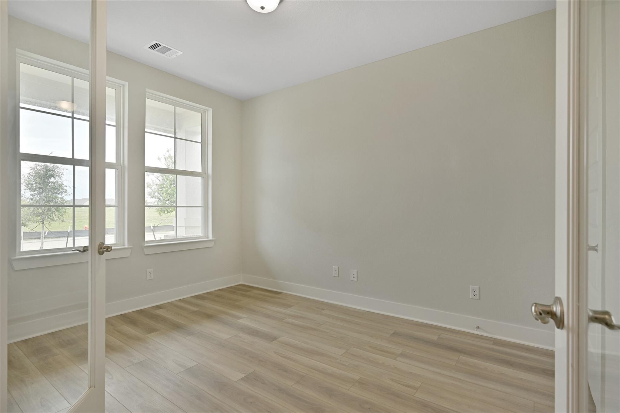 Bright secondary bedroom with large windows, beige walls, and hardwood floors in Davidson Homes The Edward A, Lago Mar, Texas City