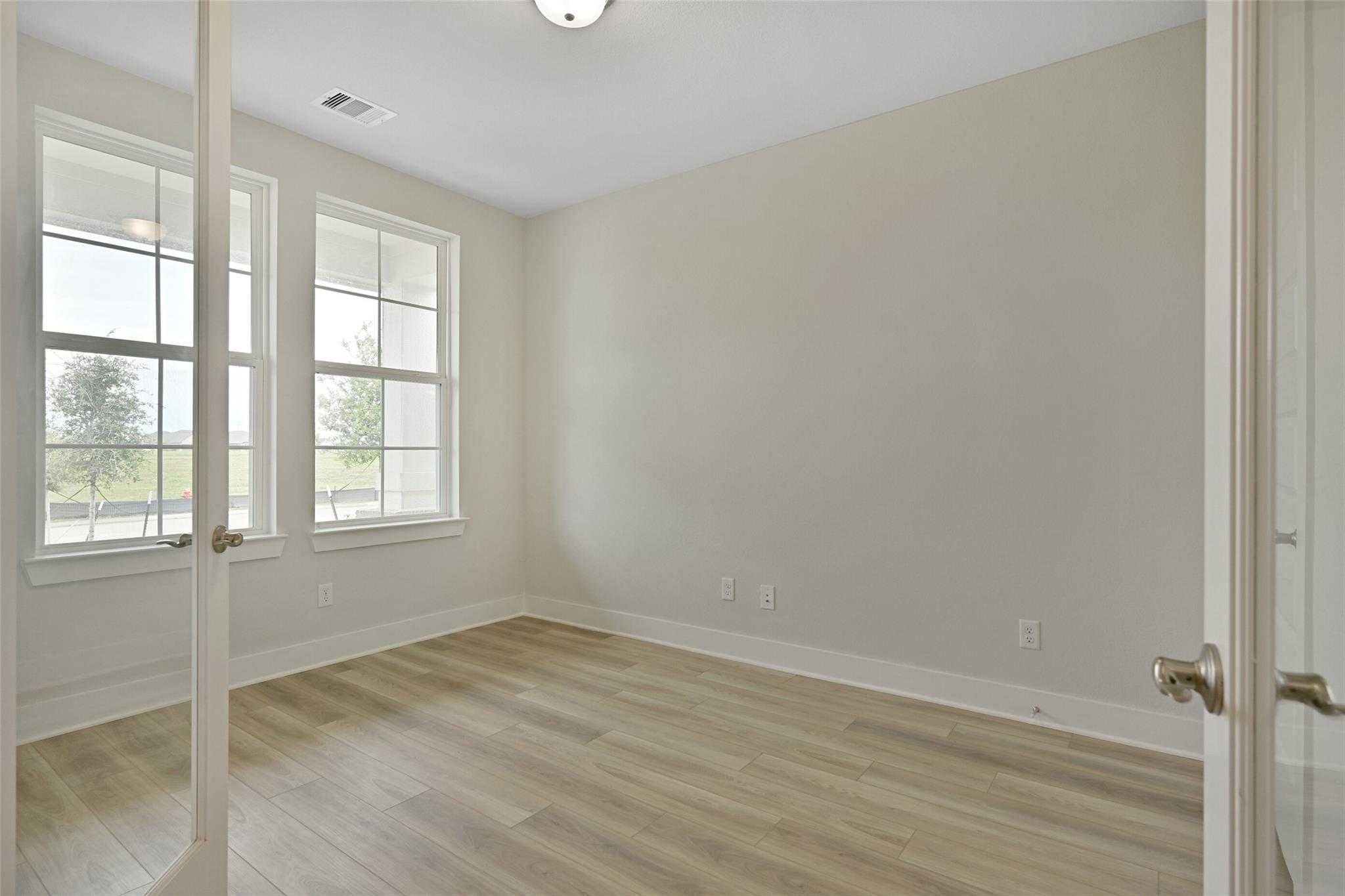 Bright secondary bedroom with large windows, beige walls, and hardwood floors in Davidson Homes The Edward A, Lago Mar, Texas City