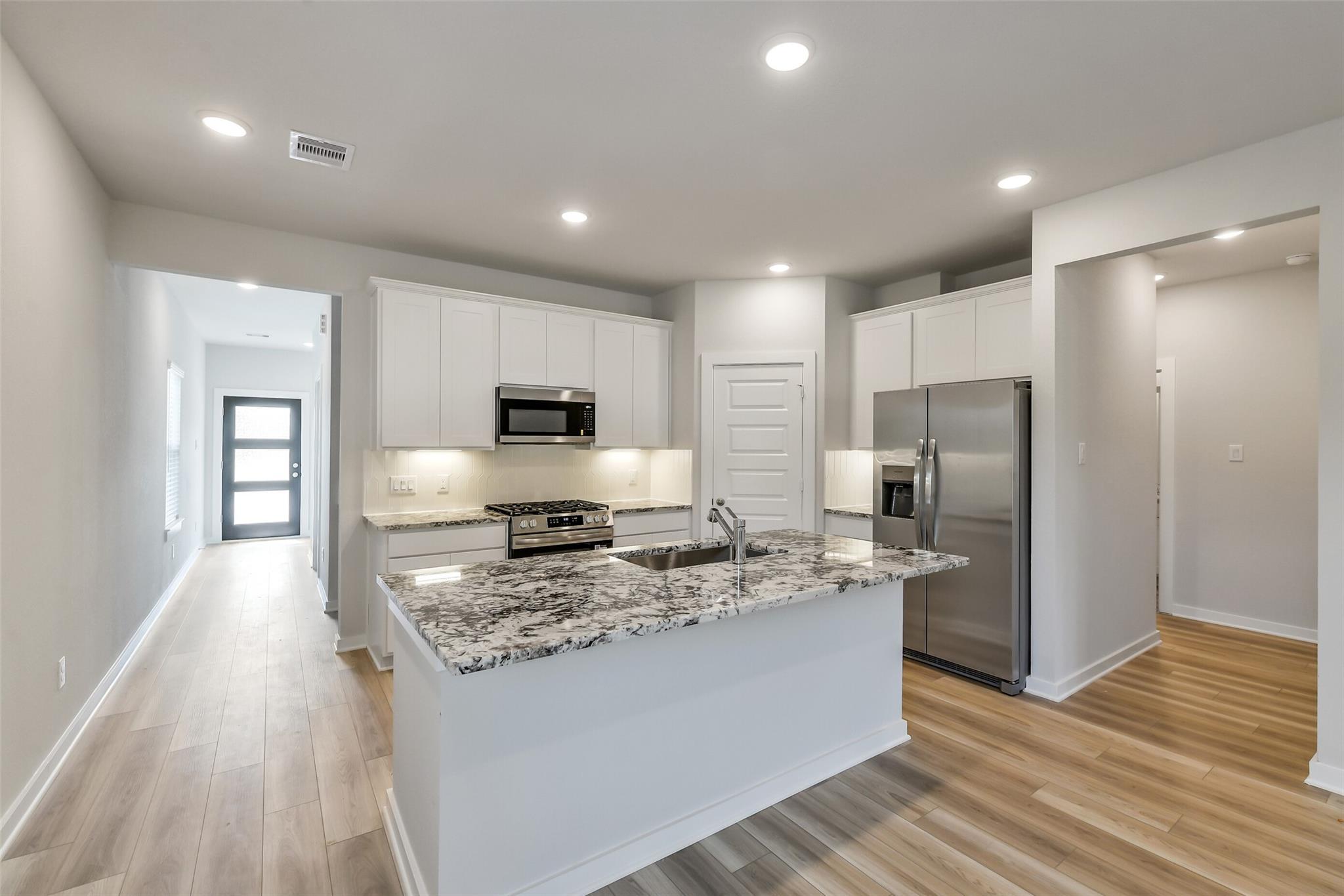 Open-concept kitchen with white cabinets, speckled granite island, stainless appliances in Davidson Homes San Marcos E, Conroe TX
