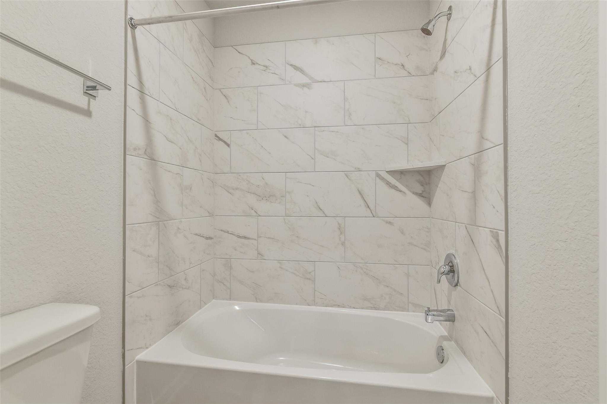 Elegant white subway tile bathroom with soaking tub, shower, and built-in shelves in Davidson Homes The Rio Grande H, Magnolia, Texas