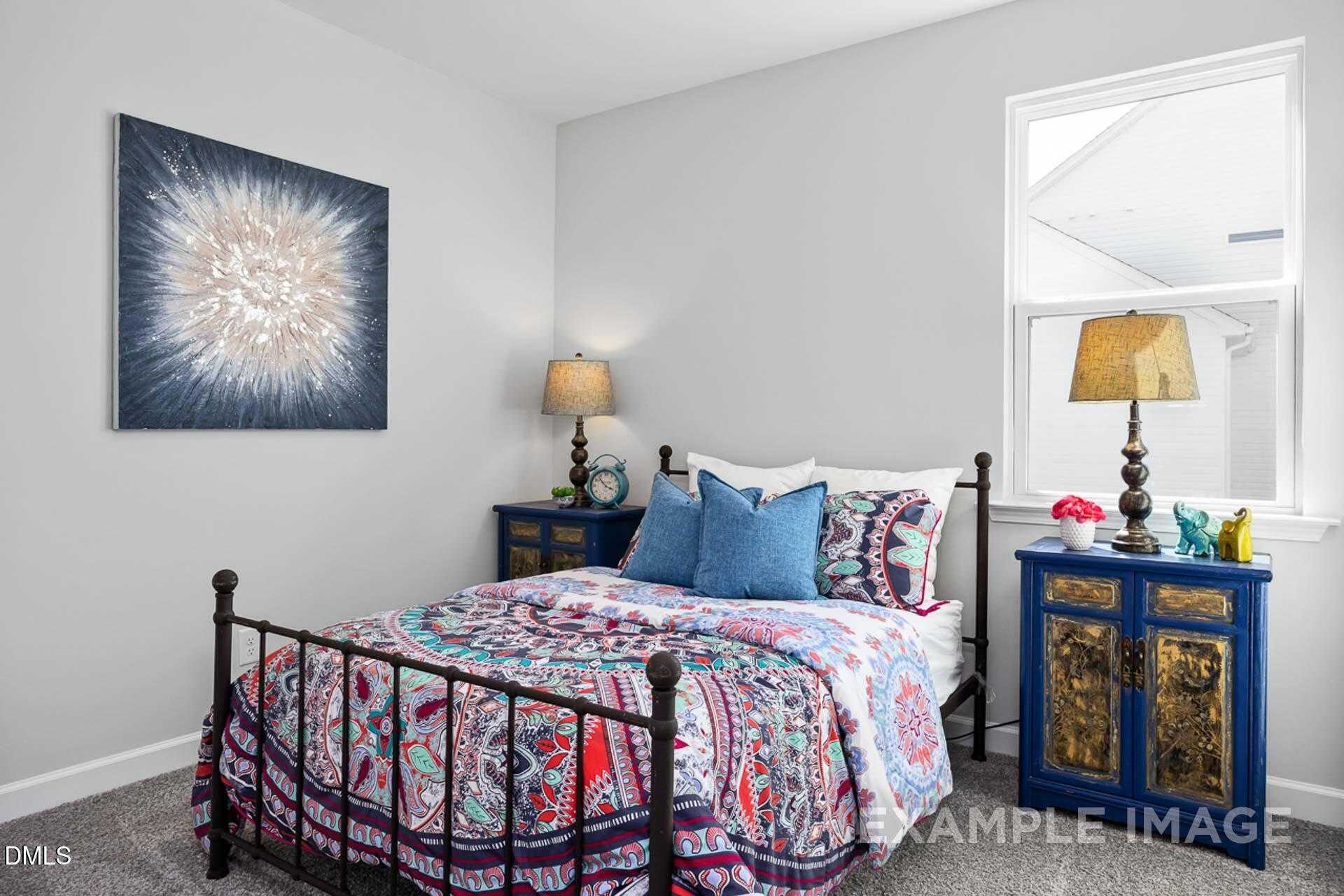 Cozy bedroom with iron bed, colorful patterned quilt, blue pillows, abstract art, and ornate nightstands in Davidson Homes The Carter C, Lillington, NC