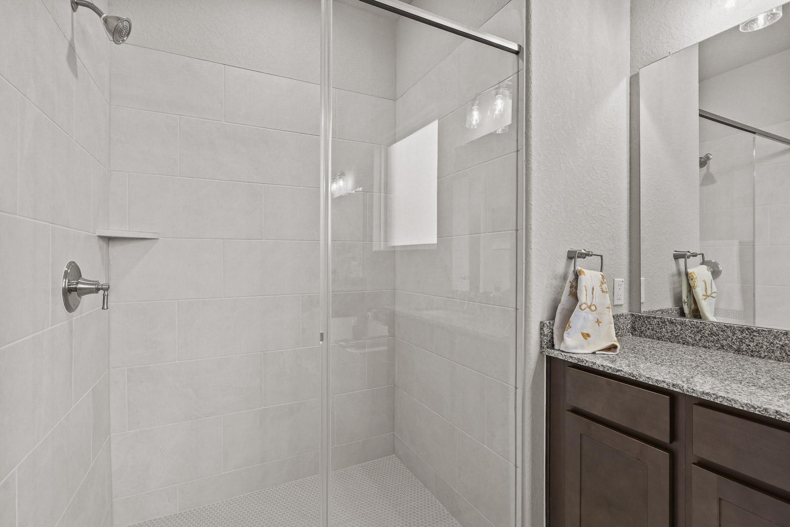 Modern bathroom in The Jennings G featuring a glass-enclosed tiled shower and granite vanity countertop.