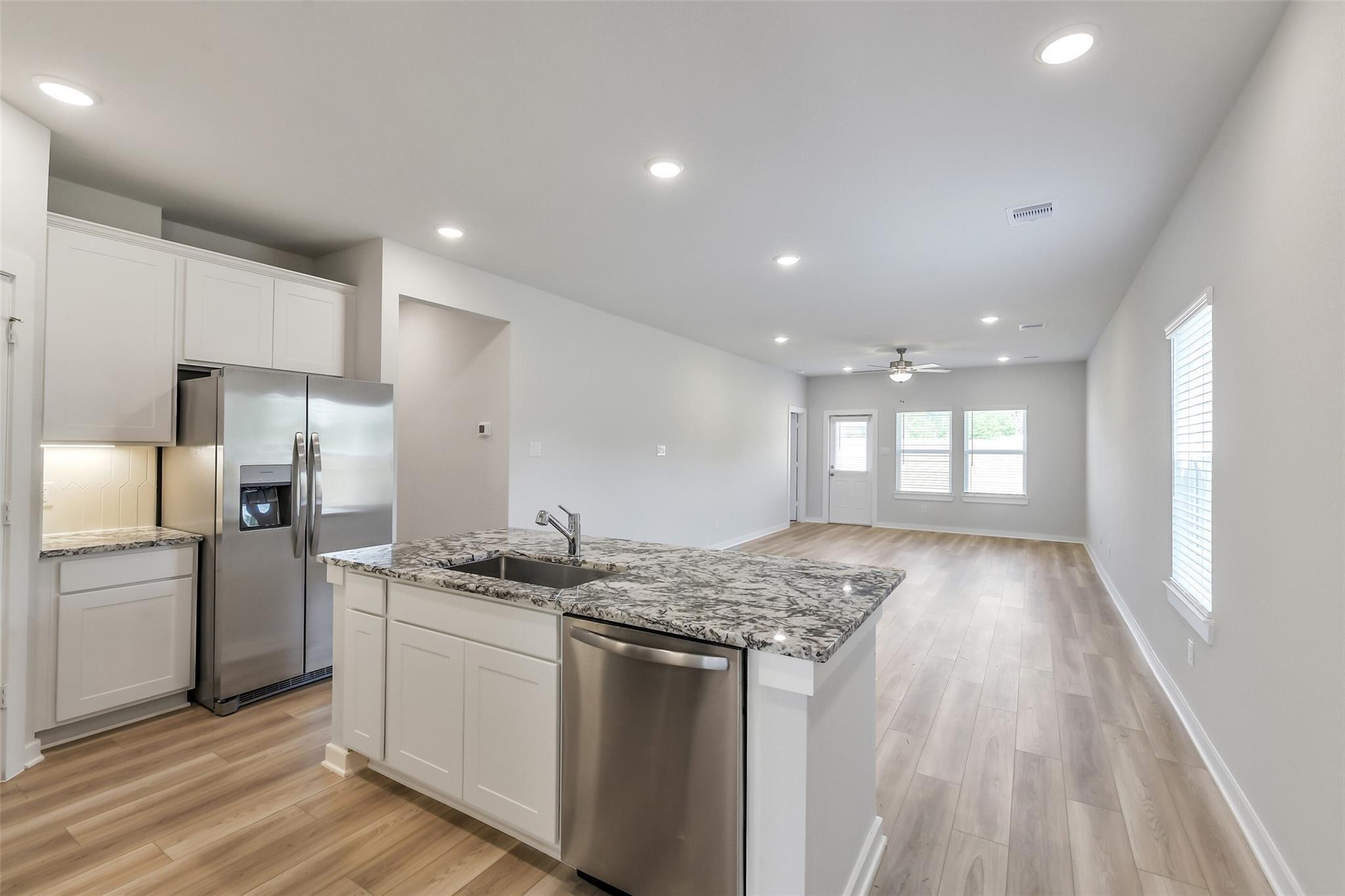 Open-concept kitchen with white cabinets, granite island sink, stainless fridge and dishwasher in Davidson Homes San Marcos E, Conroe TX