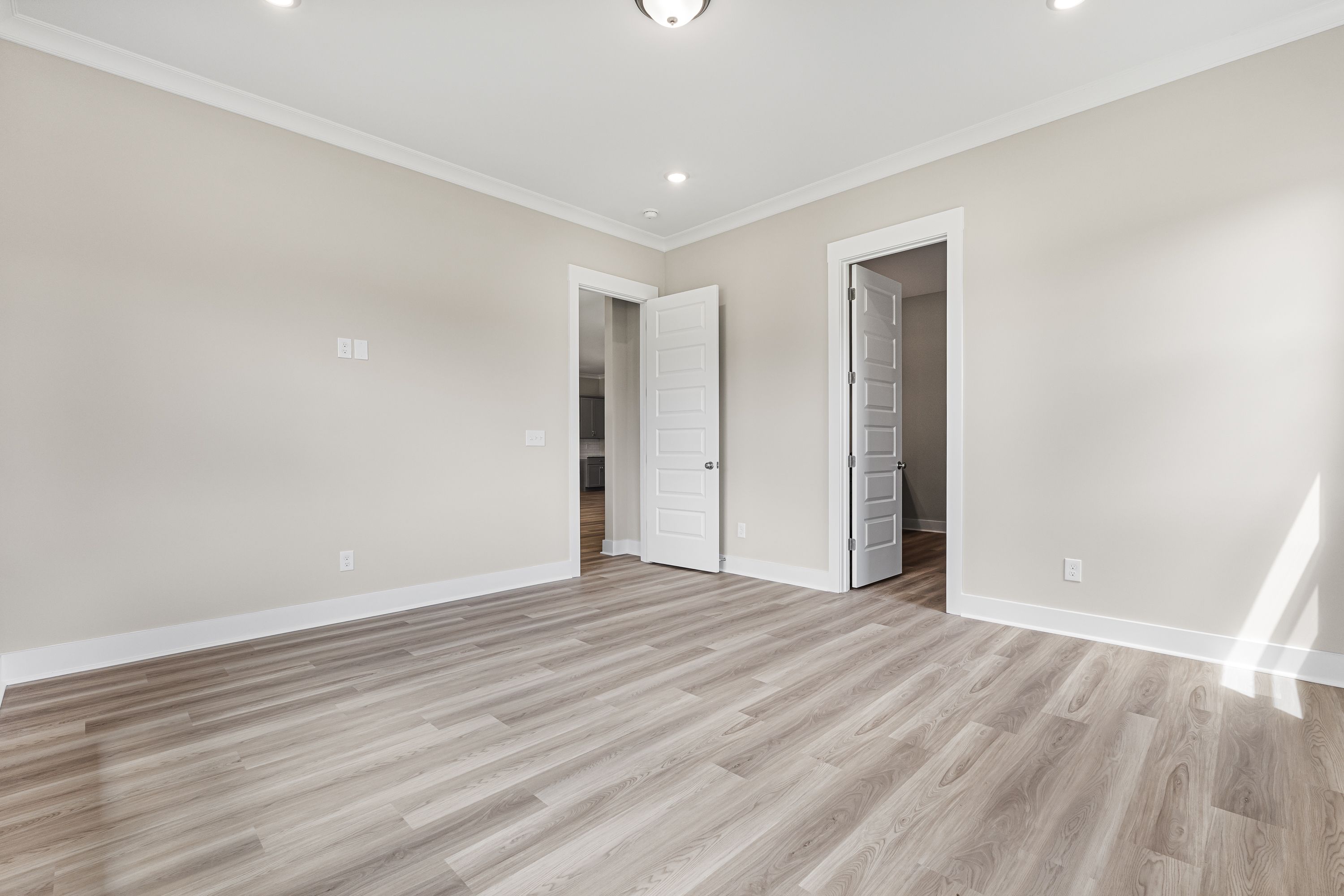 Spacious empty bedroom in The Oxford A home featuring beige walls, light oak flooring, open doors to ensuite bath