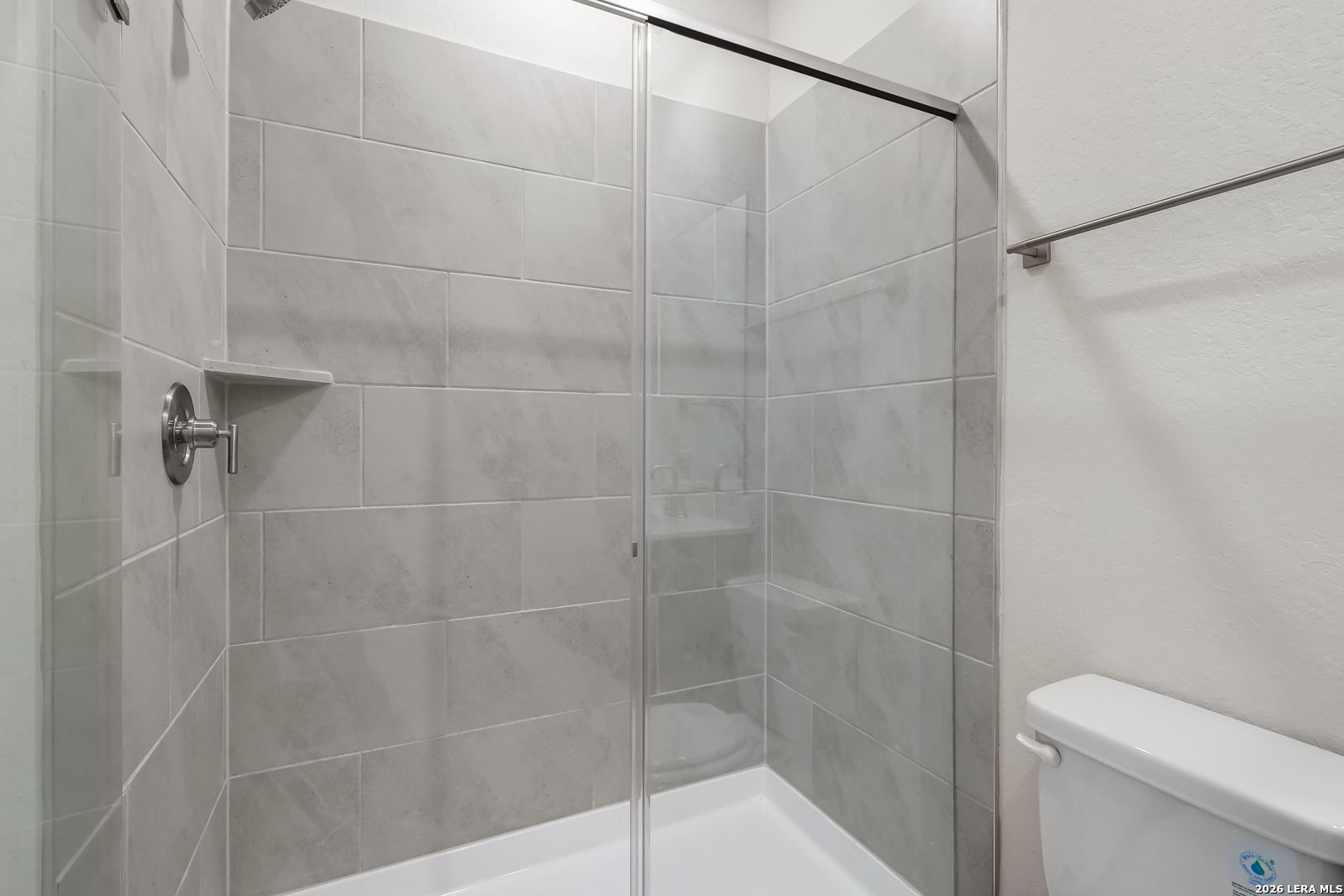 Modern walk-in shower with gray tile surround and glass door in Davidson Homes San Marcos F floor plan, San Antonio.