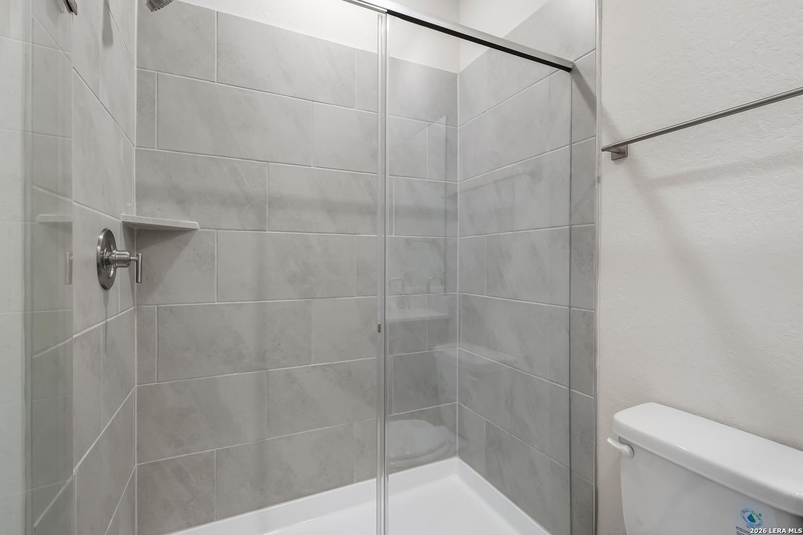 Modern walk-in shower with gray tile surround and glass door in Davidson Homes San Marcos F floor plan, San Antonio.