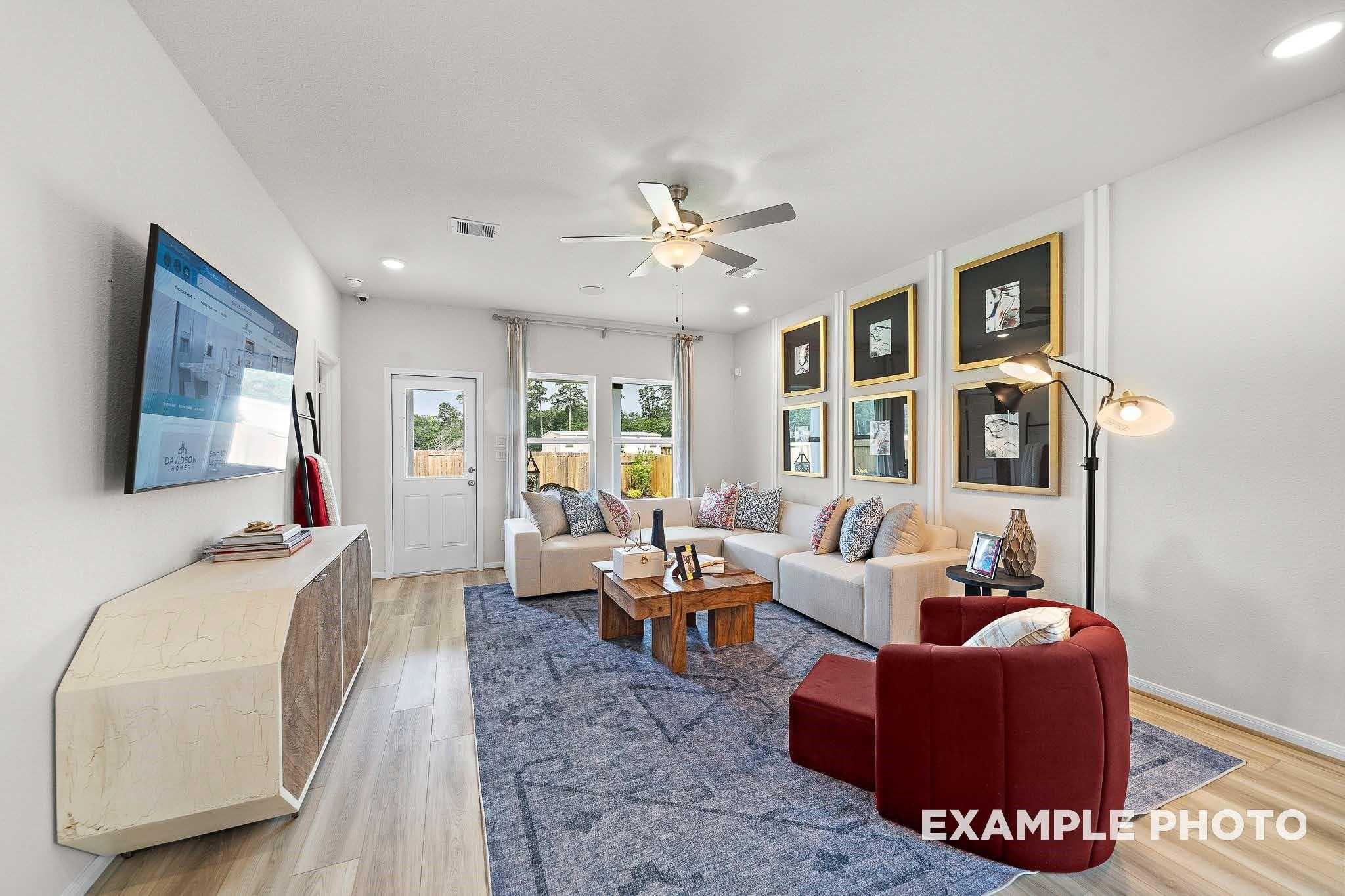 Spacious living room with beige L-shaped sofa, red armchair, wooden coffee table, and French doors in Davidson Homes San Marcos E, Conroe TX