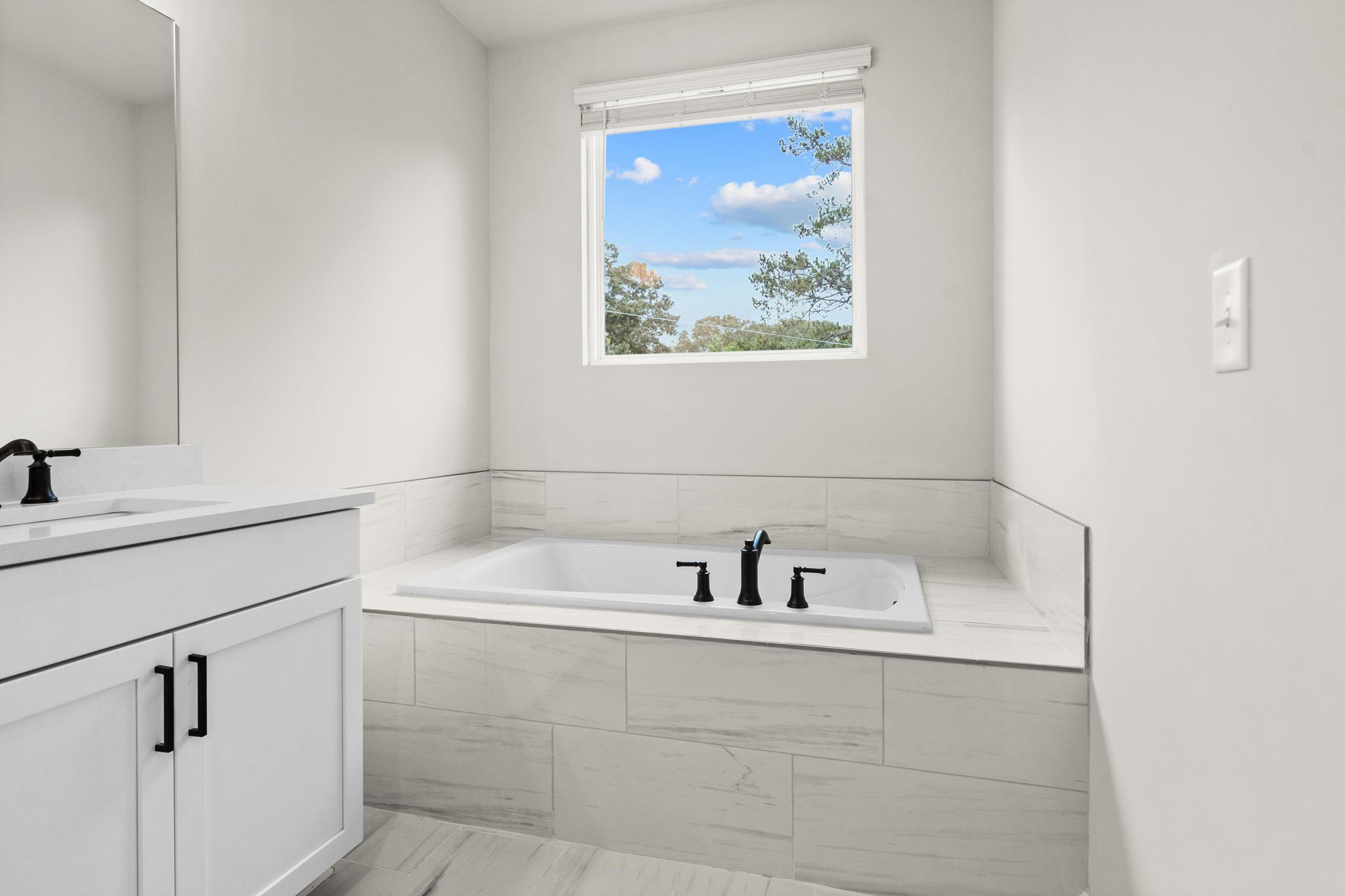 Spacious master bathroom in The Glenwood featuring soaking tub, white vanity, and window with tree view