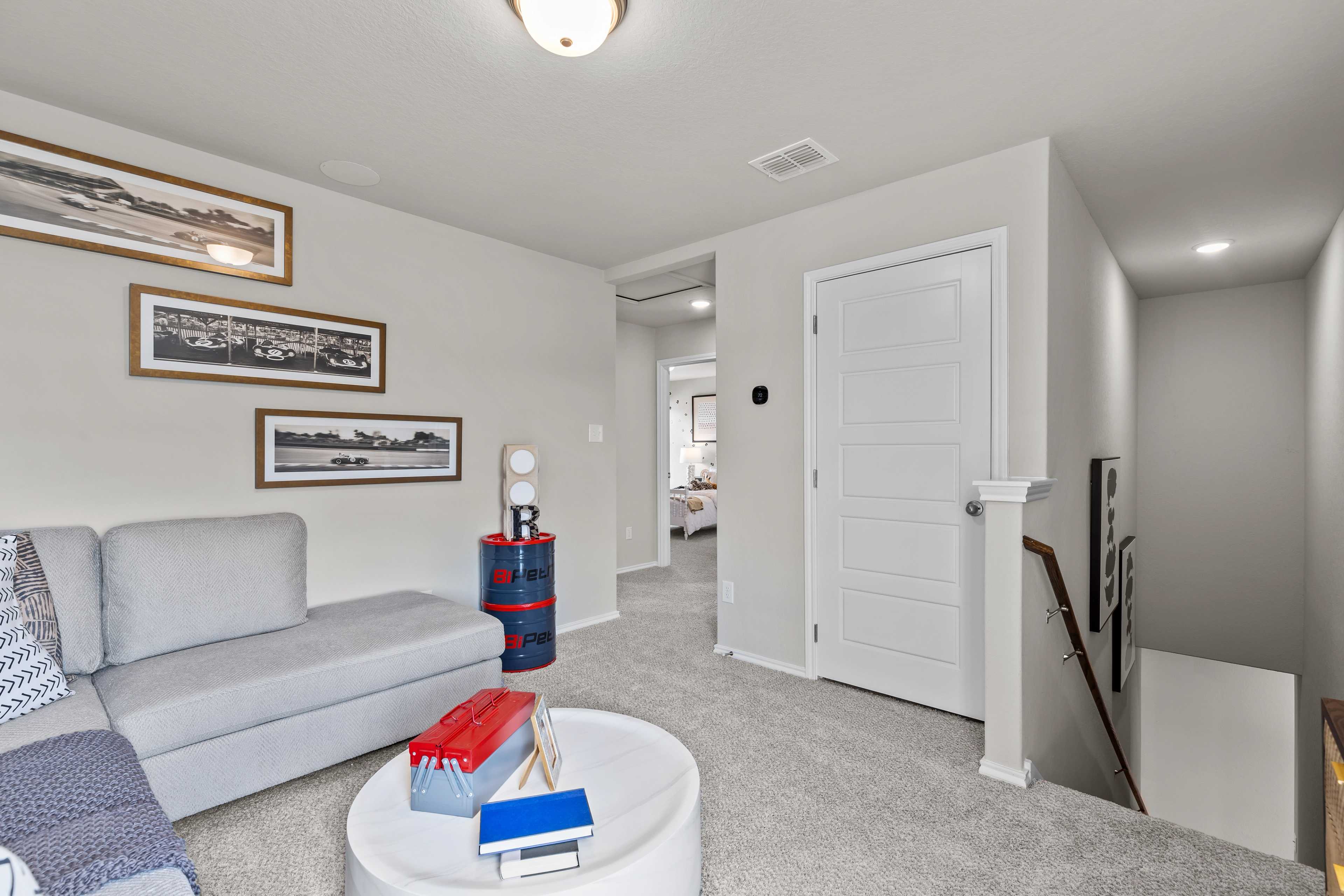 Spacious upstairs loft in The Sabine C Davidson Homes plan: gray sofa, white coffee table, framed art, open bedroom doorway