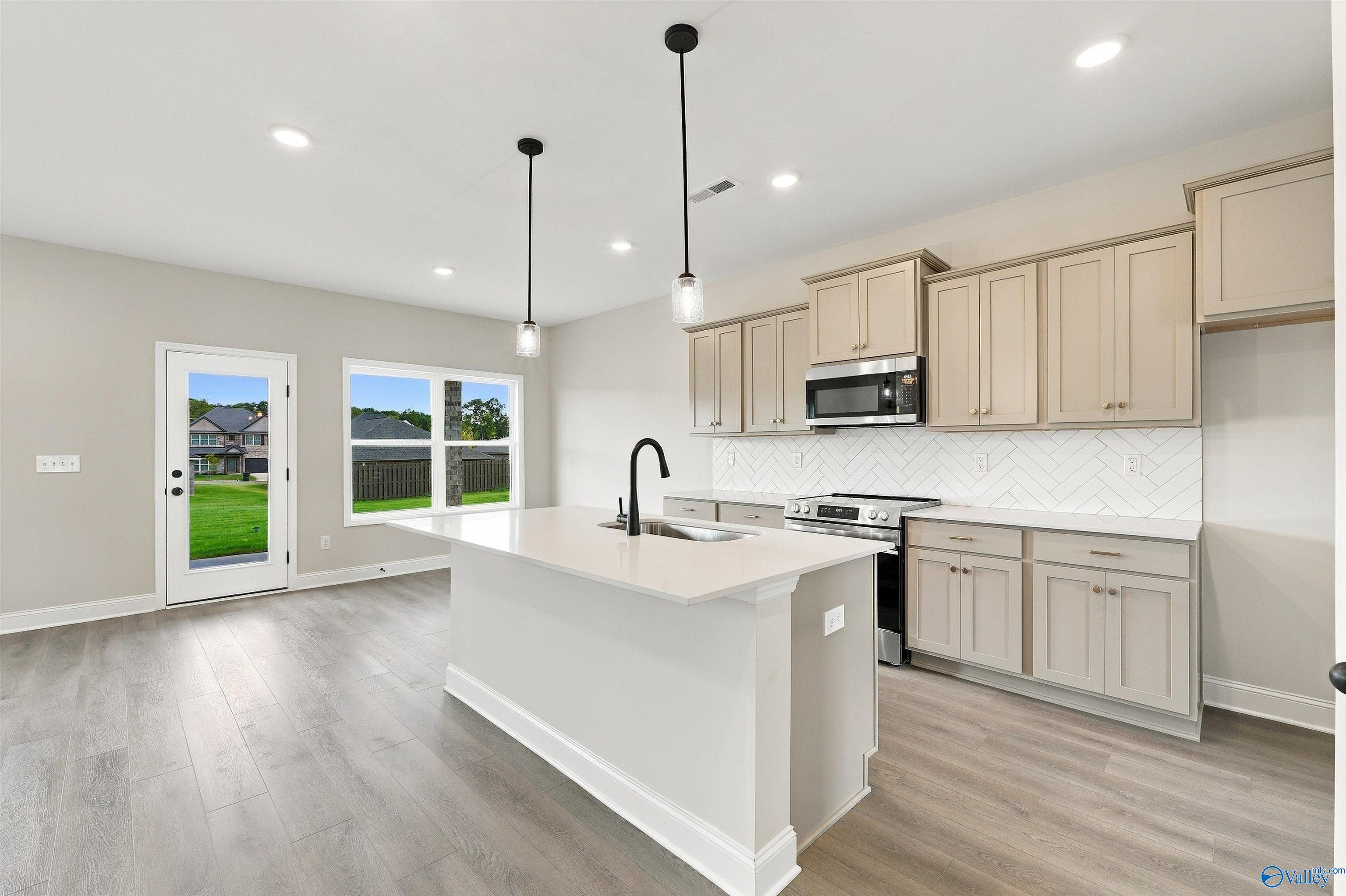 Kitchen island with pendant lights and beige cabinets in Davidson Homes The Shelby A floor plan, The Meadows, Athens, Alabama
