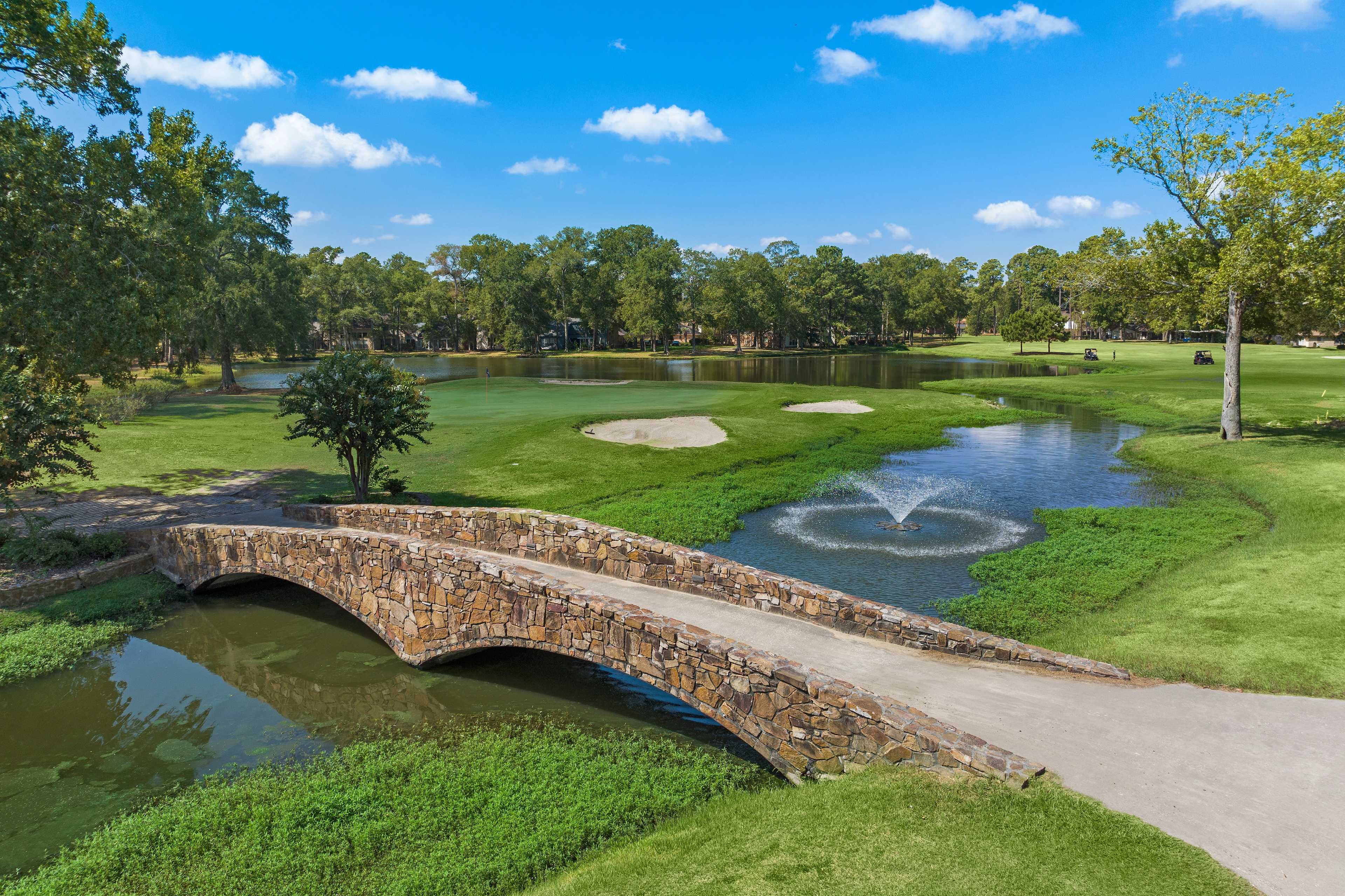 Aerial view of stone arch bridge over pond with fountain on lush golf course at Enclave at Newport in Crosby, Texas