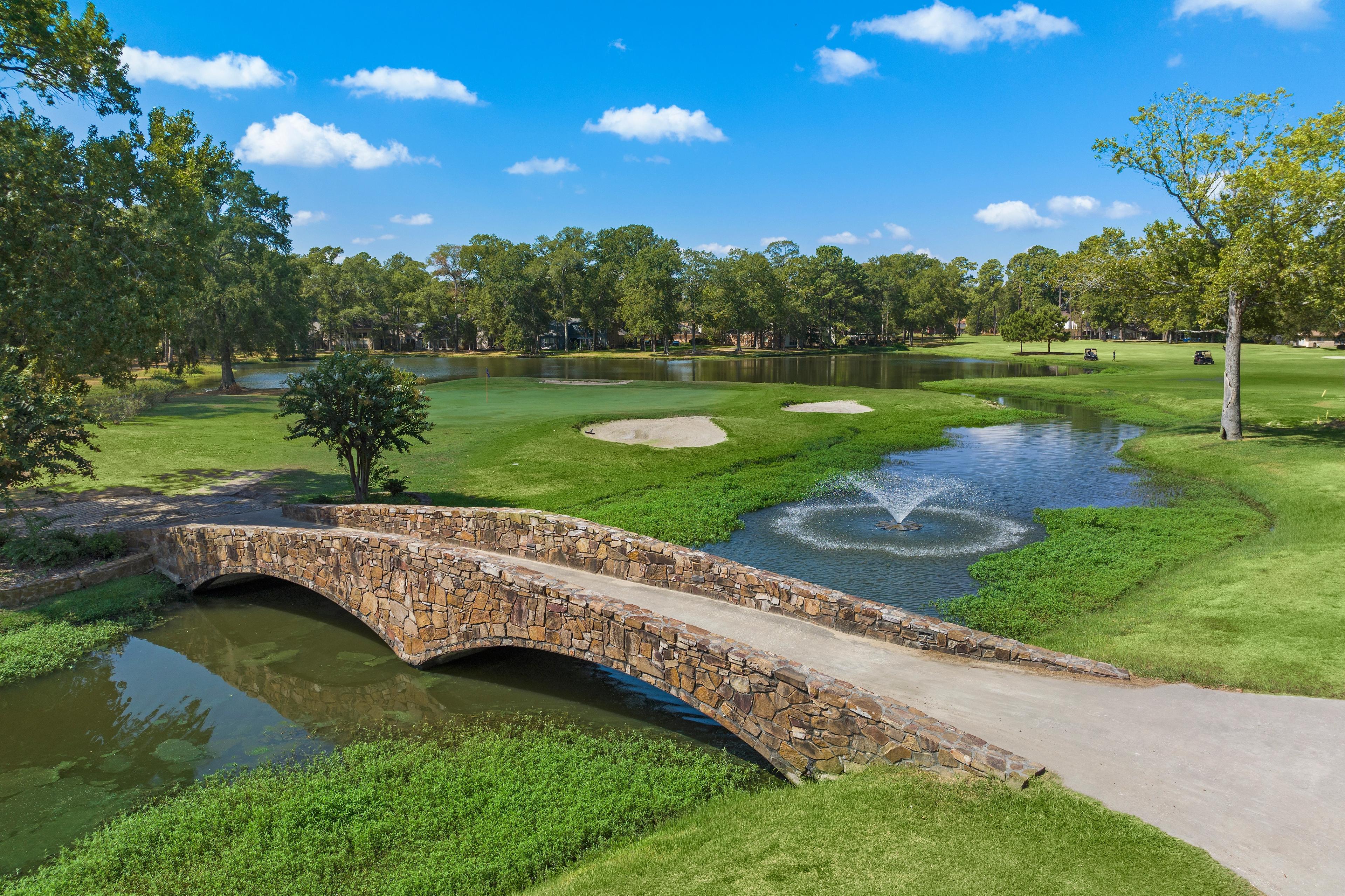 Aerial view of stone arch bridge over pond with fountain on lush golf course at Enclave at Newport in Crosby, Texas