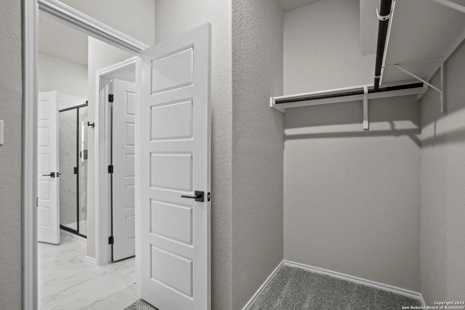 Spacious walk-in closet with hanging rod and shelves adjacent to master bath with glass shower in Davidson Homes The Asheville E, Converse, Texas